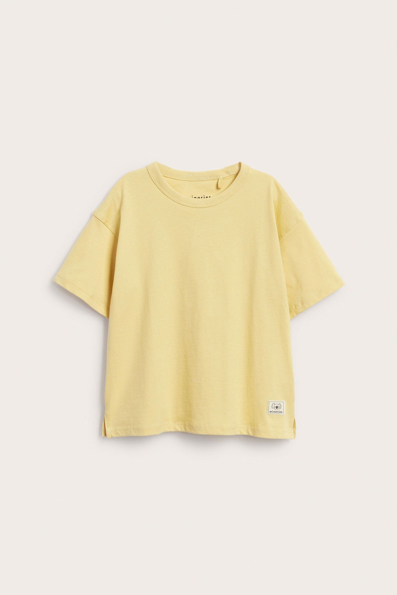 Frontvy av en enfärgad gul kortärmad T-shirt i bomull för barn med ett vävt märke.