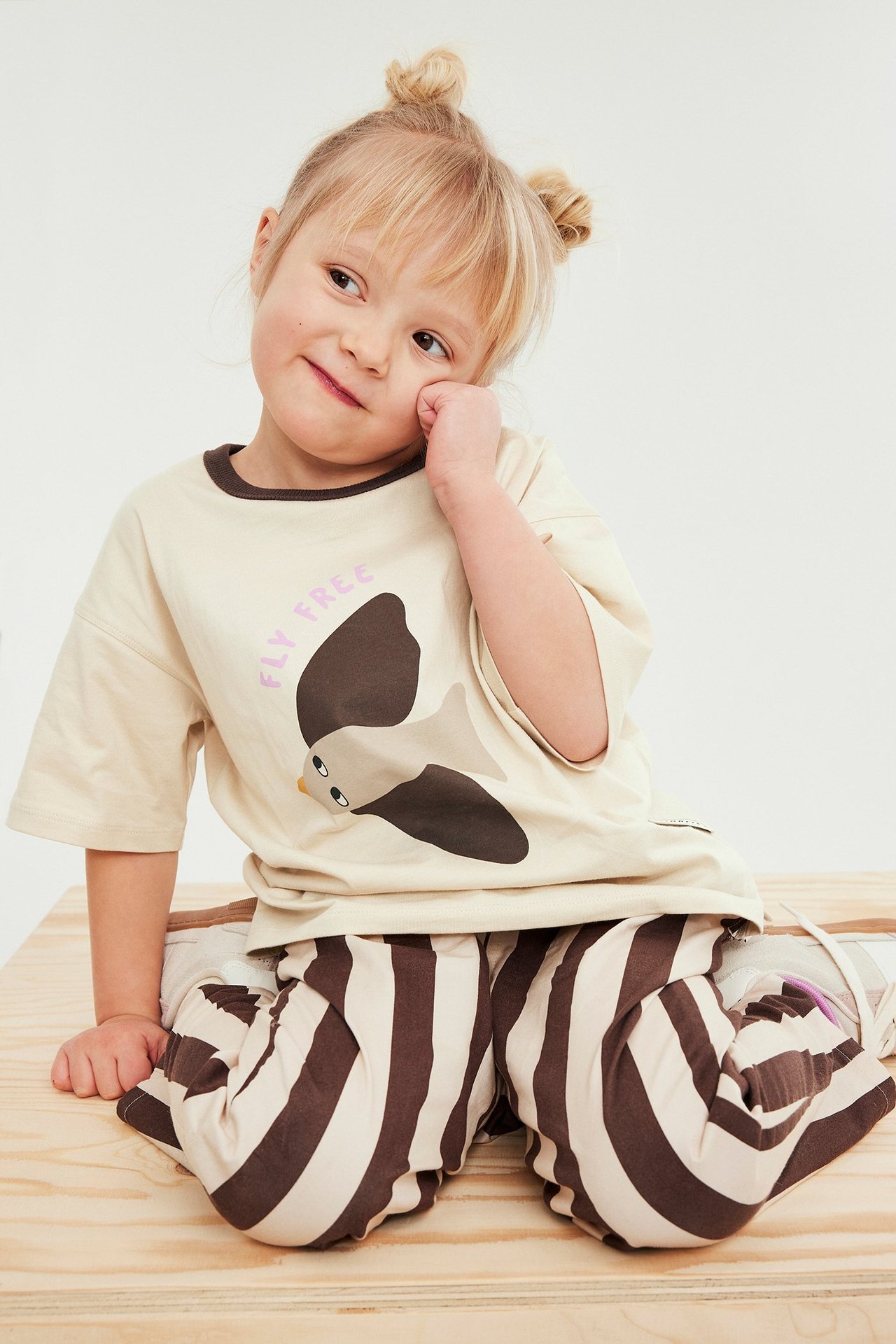 Edestäpäin: Lapsi yllään väljä beige puuvillainen t-paita lintupainatuksella ja raidalliset housut.