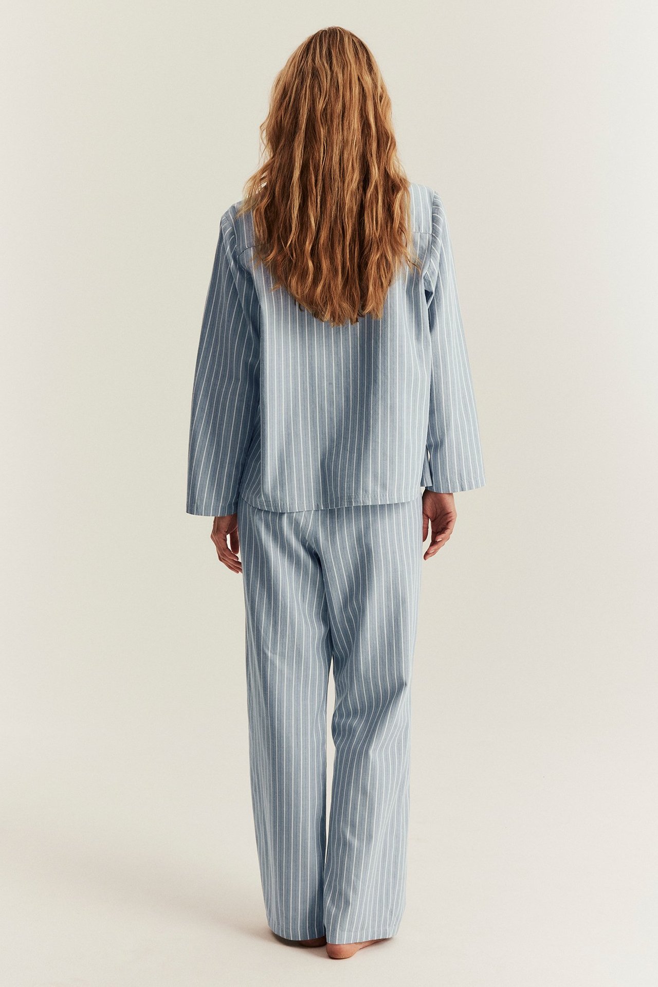 Ryggbilde av en kvinne i en løstsittende lyseblå og hvitstripete bomullspysjamas.