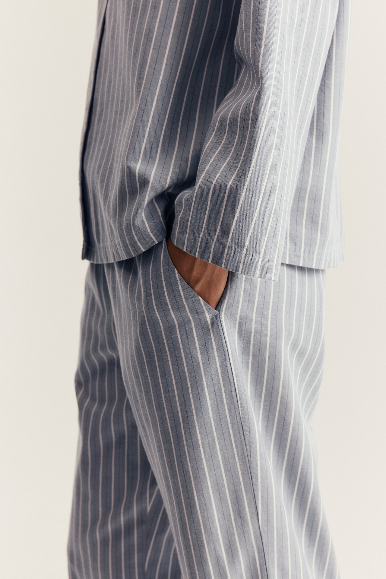 Sidovy av kvinna i ljusblå-vitrandig pyjamas i bomull, handen i byxfickan.