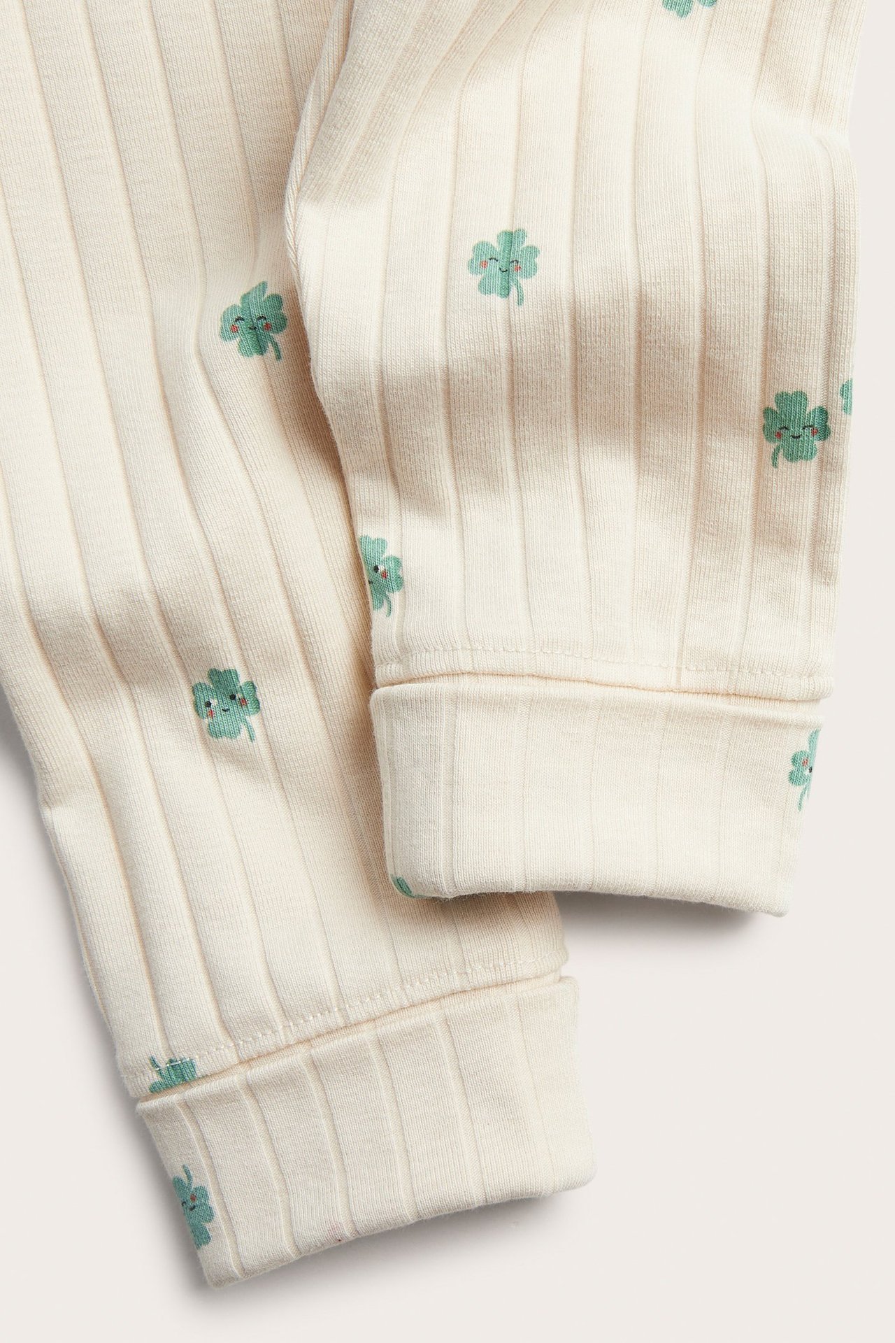 Zbliżenie beżowych prążkowanych legginsów niemowlęcych z zielonym wzorem koniczyny i podwijanymi mankietami.