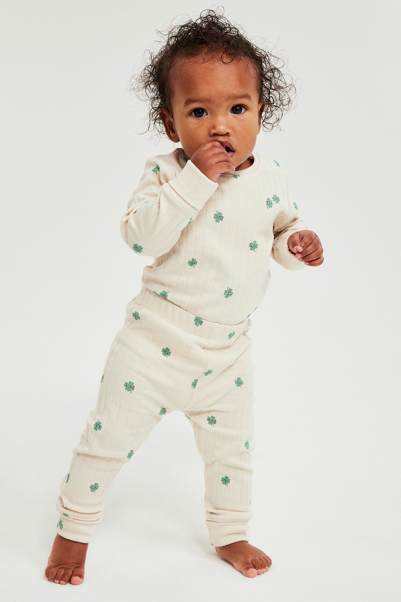 Edestä: Vauva beigessä ribbileggingsissä vihreällä apilakuviolla ja yhteensopivassa yläosassa.