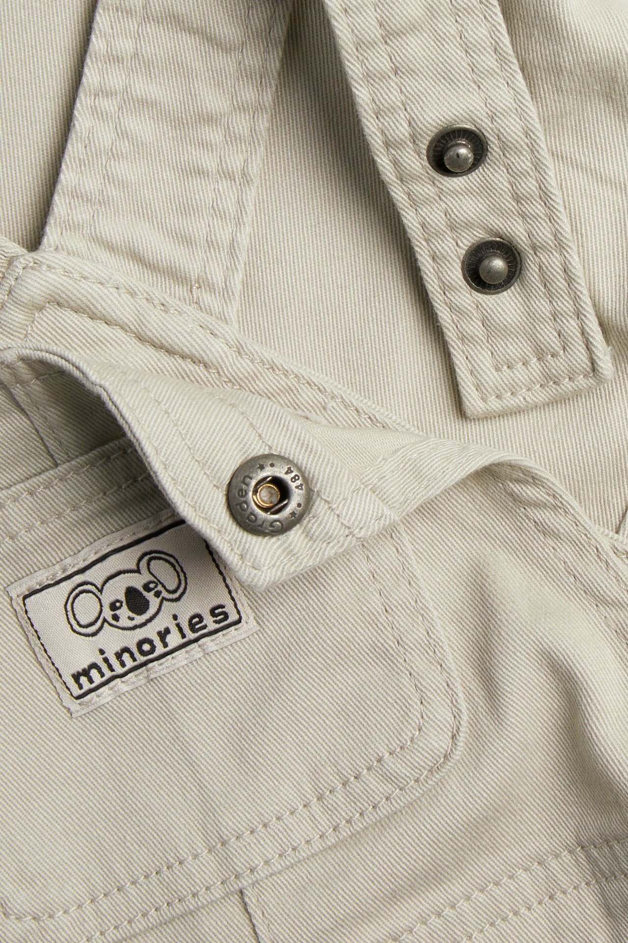 Beiget twilli-hängleshousut lapsille, säädettävät hihnat, logo rinnataskussa, napit.