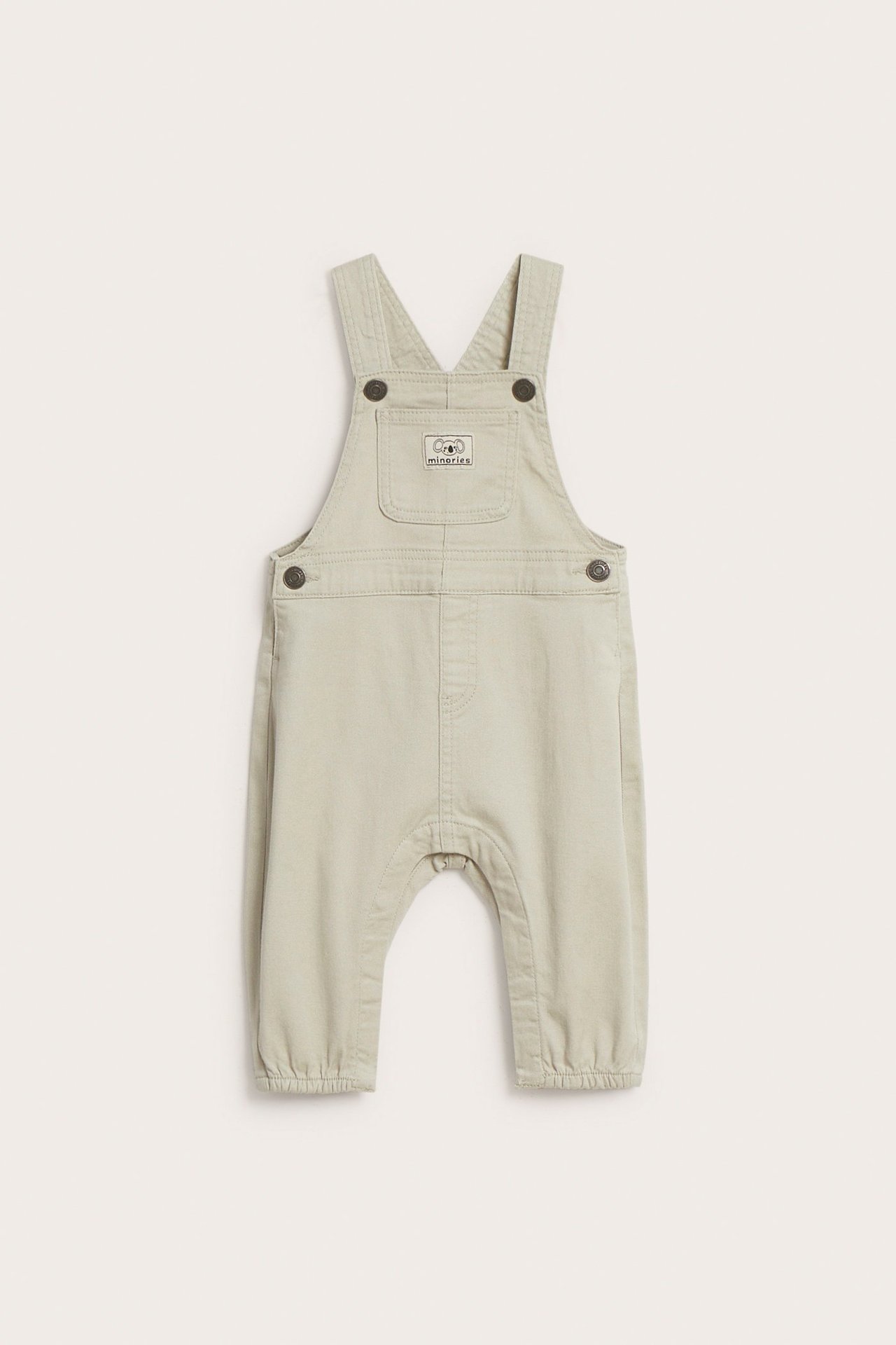 Beige twill-hengelliset housut säädettävillä hihnoilla ja Minories-logolla.