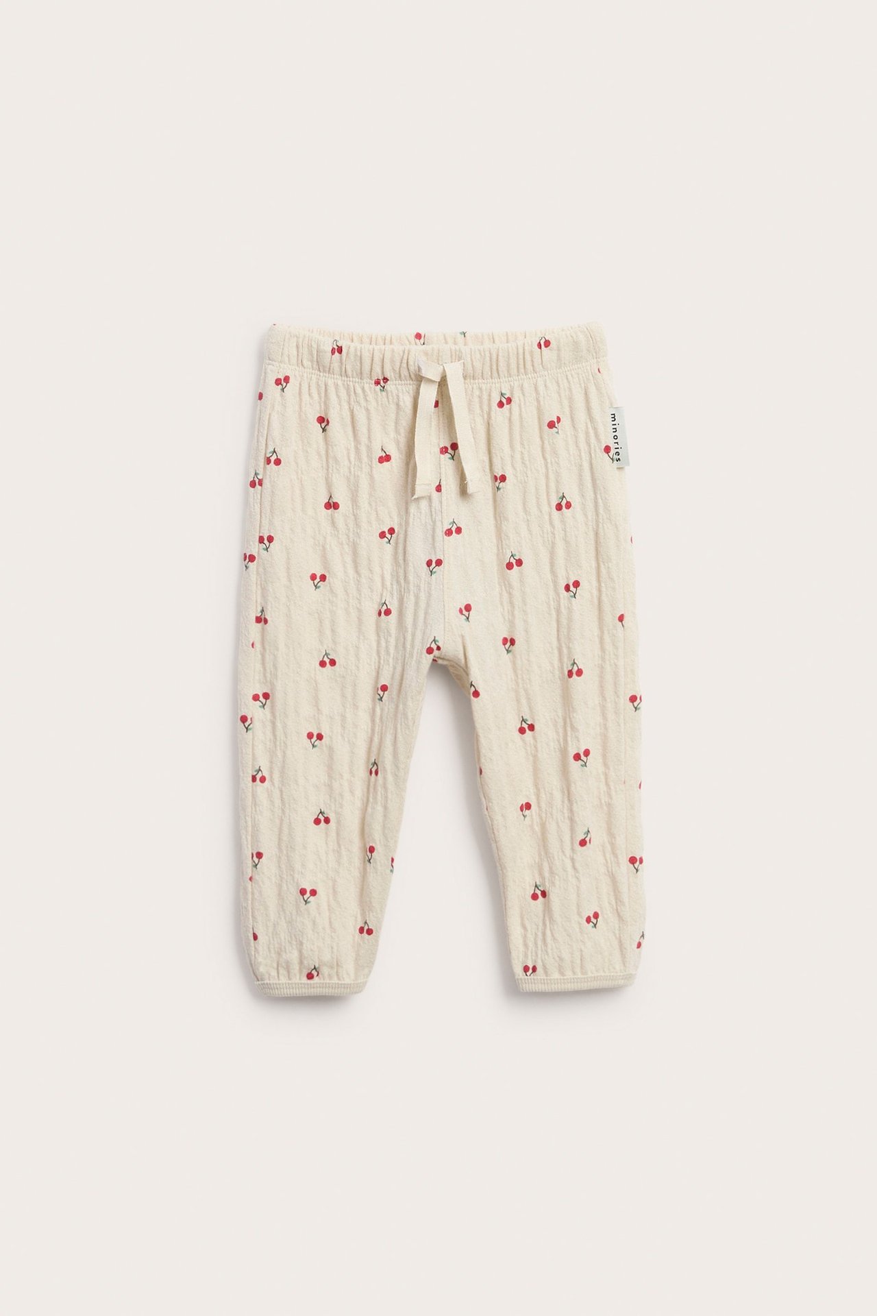 Frontvy av ljusbeige babyjoggingbyxor med körsbärsmönster, resårmidja och dragsko.