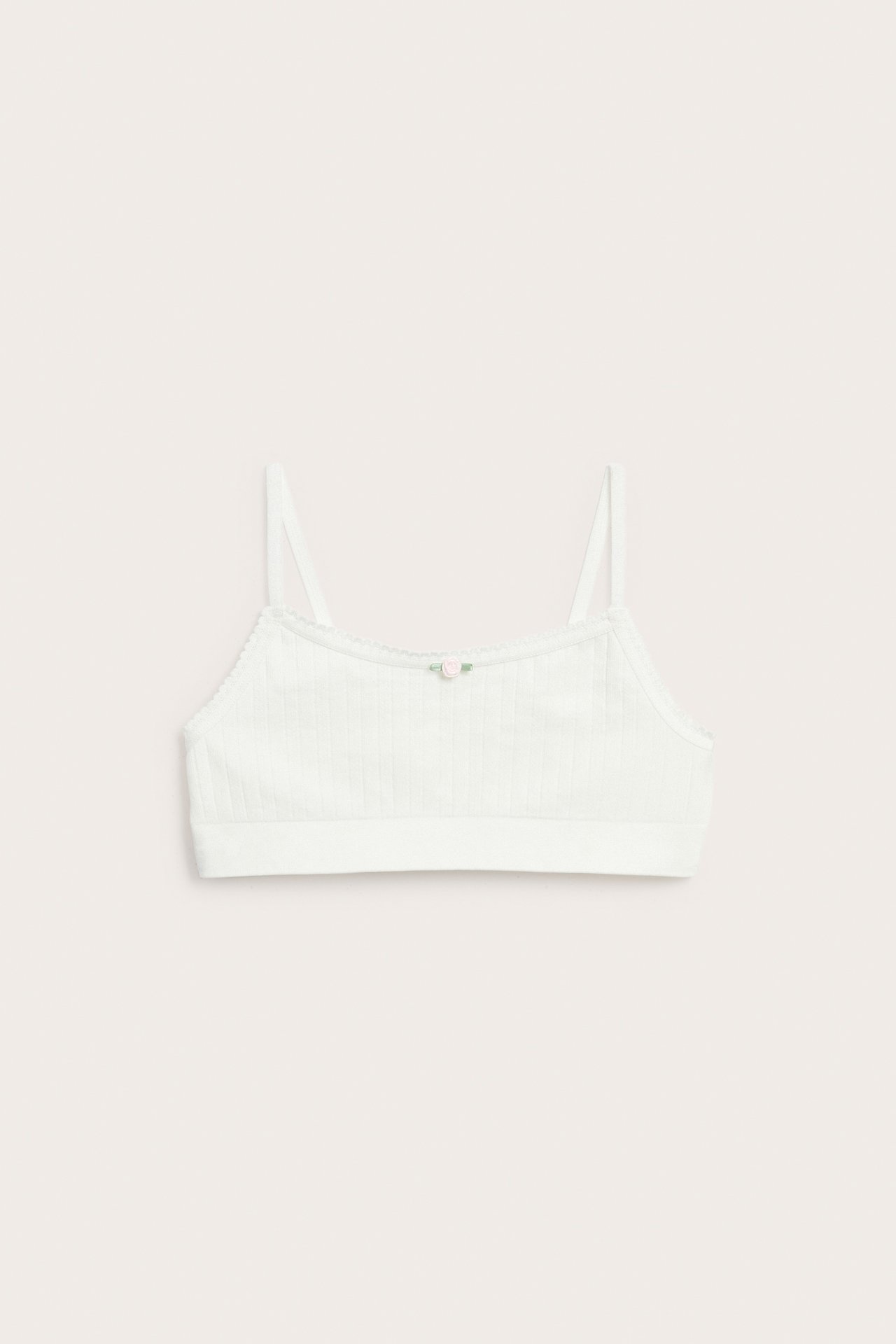 Widok z przodu: top bezszwowy pointelle w kolorze ecru z cienkimi ramiączkami i małą różową różą.