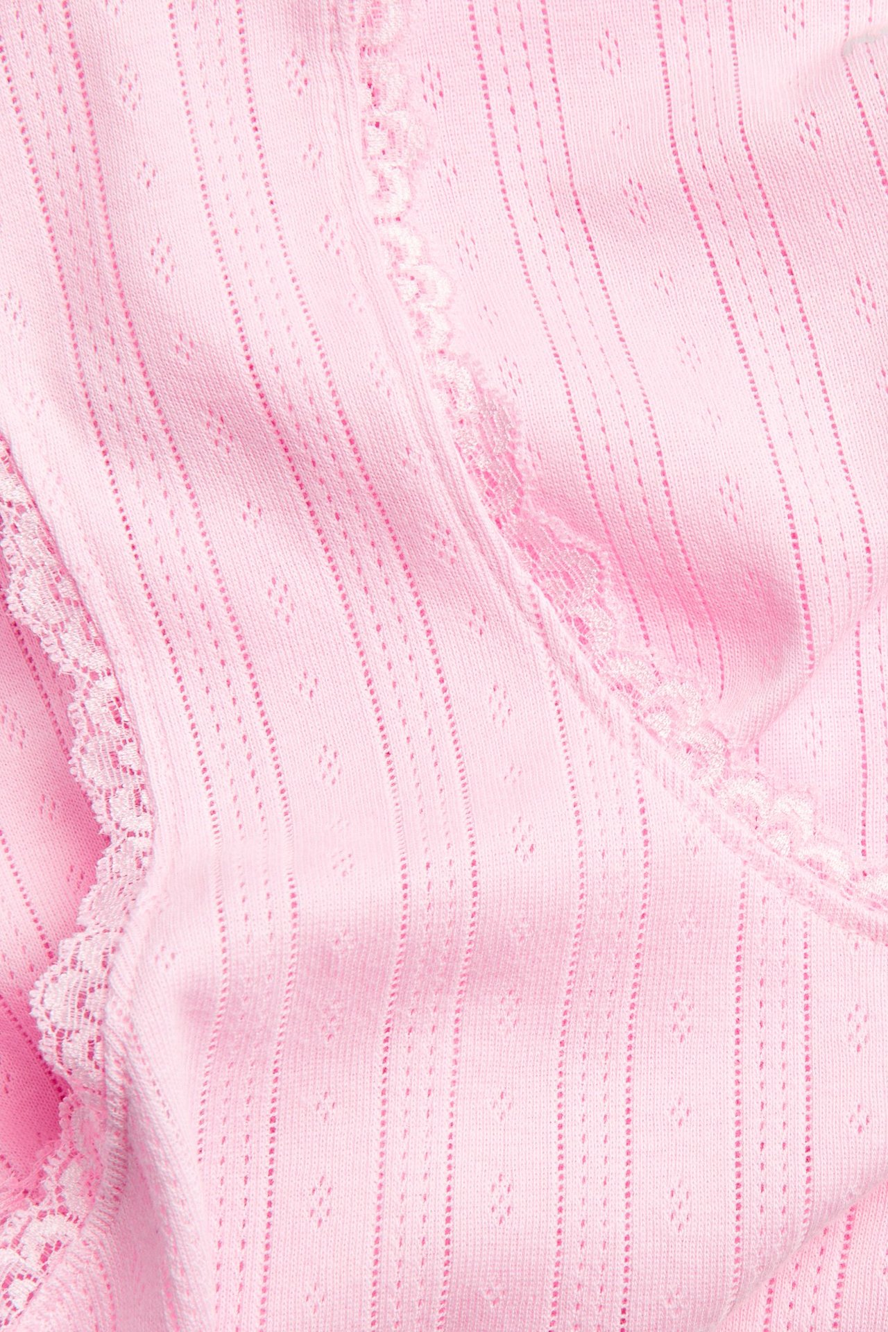 Närbild av en rosa pointelle pyjamaslinne med strukturerat mönster och vit spetskant.