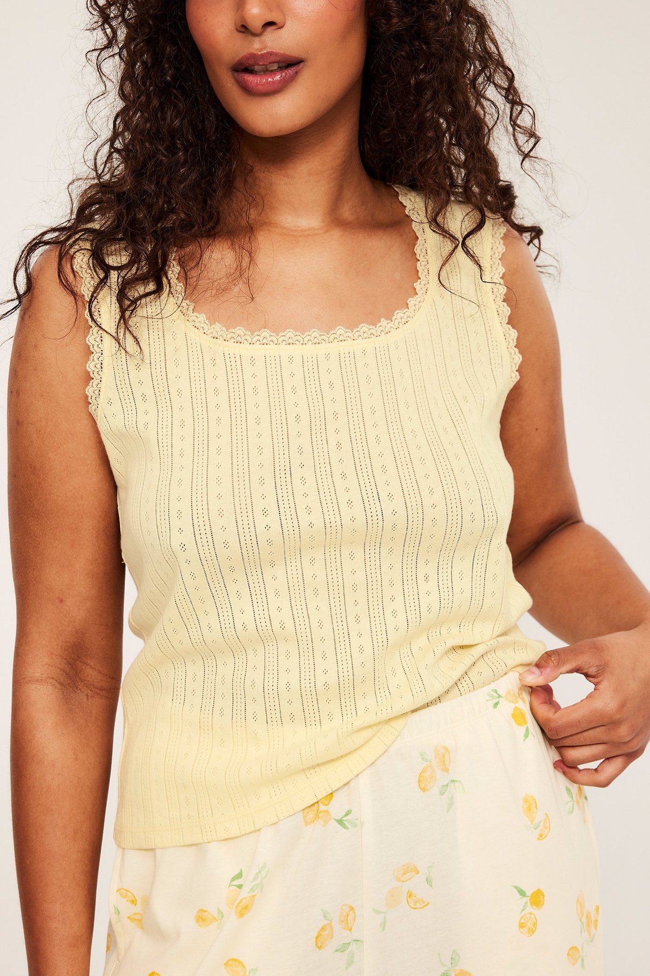 Edestä: nainen keltaisessa pointelle-pyjamatoppissa, jossa pitsireunus, yhdistettynä sitruunakuviollisiin pyjamashortseihin.