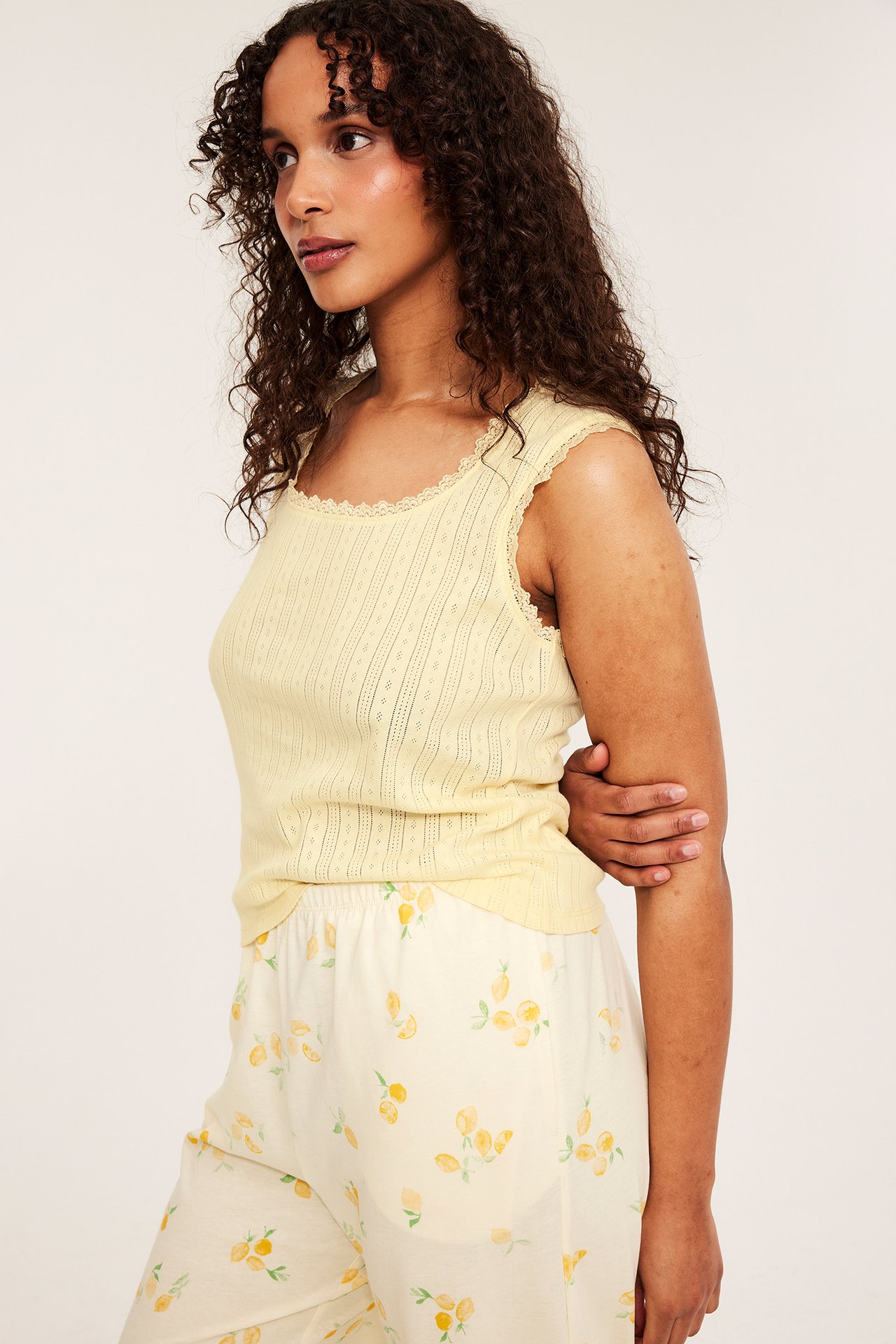 Kvinnes gul pointelle pyjamastopp med blondekant, stylet med kremfargede sitronmønstrede shorts, sideutsikt.