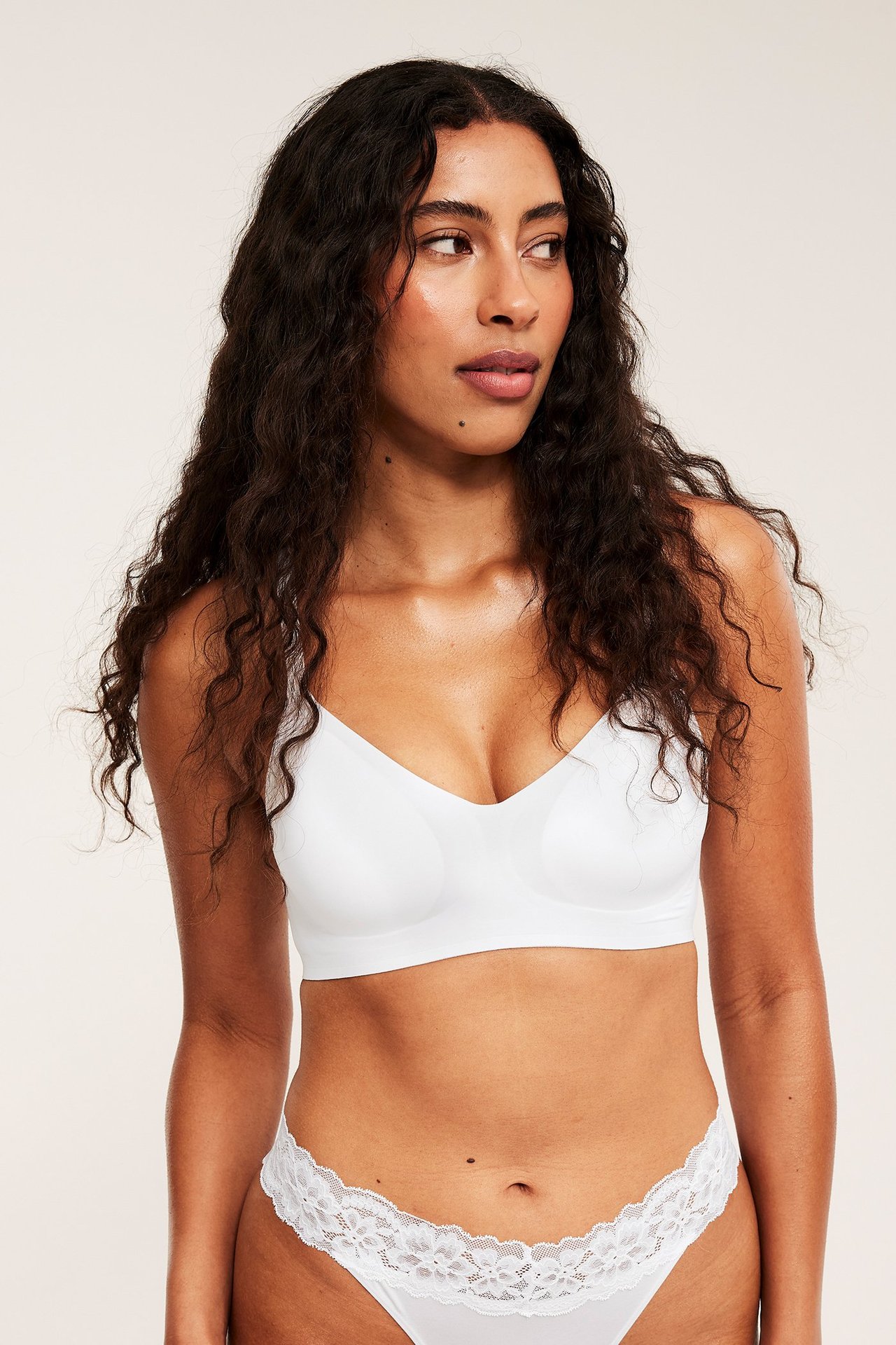 Framifrån, kvinna i en vit supermjuk bygellös V-ringad BH och vita spetskantade trosor.