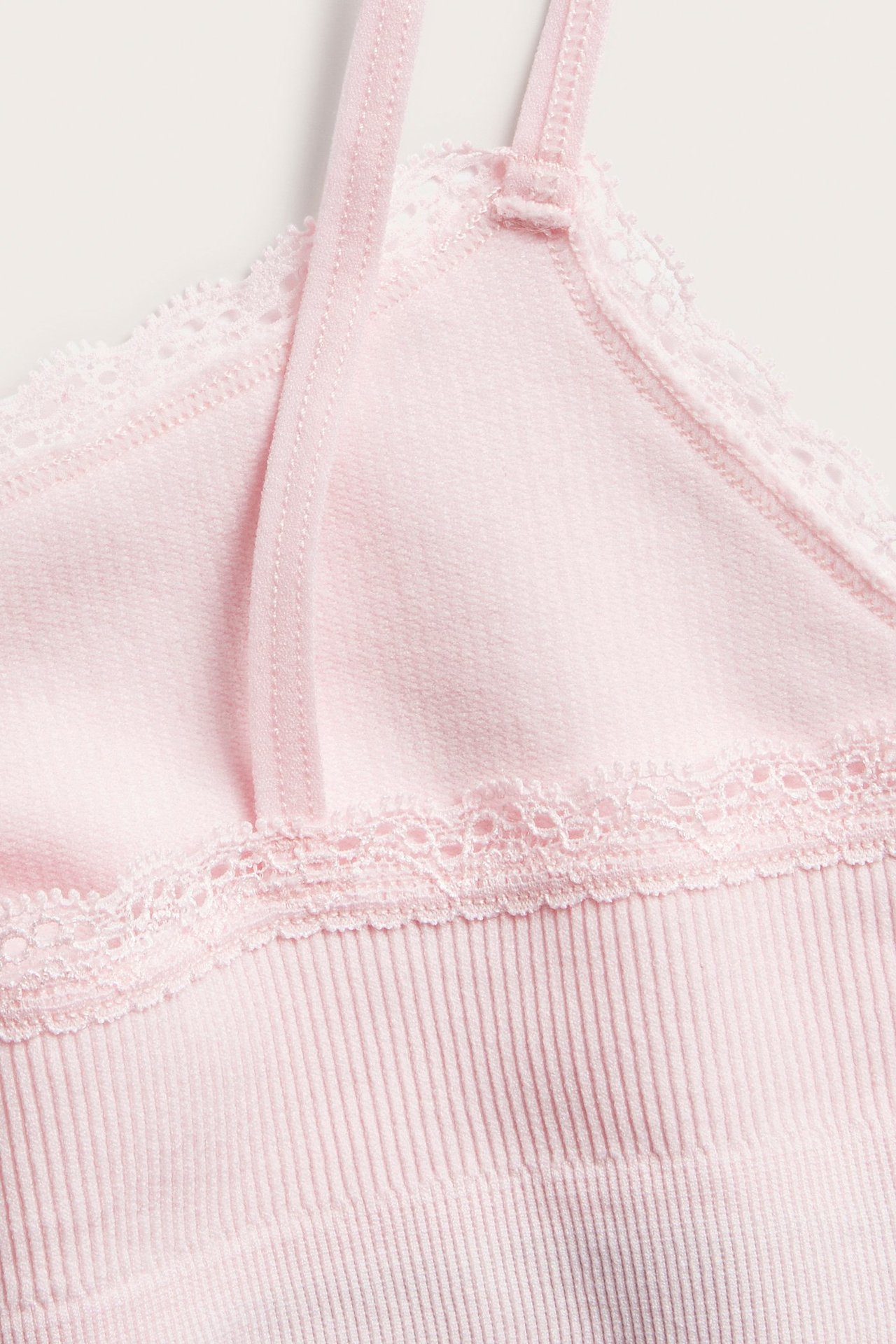 Närbild av en rosa seamless ribbad topp med delikata spetsdetaljer och justerbara axelband.