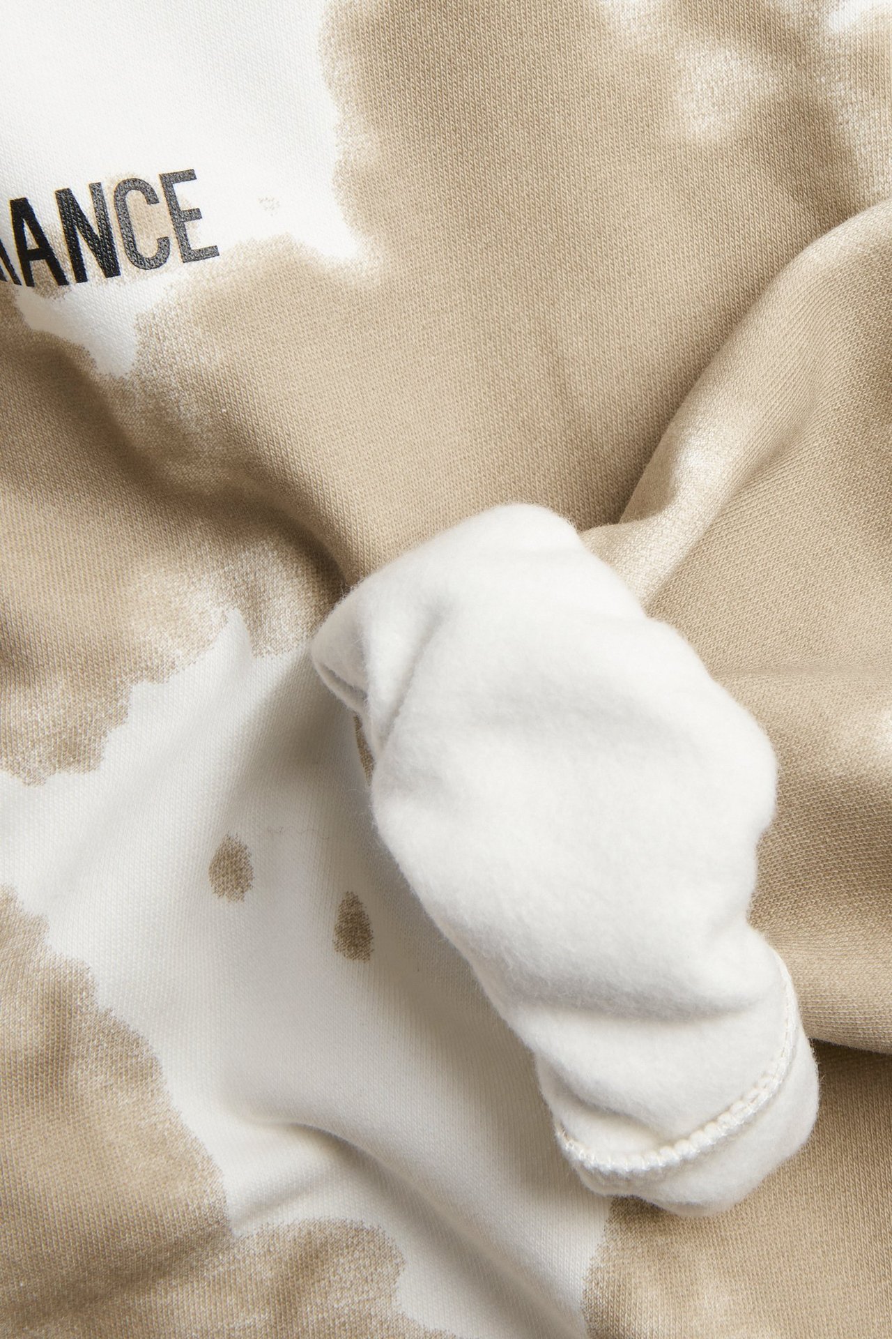 Zbliżenie biało-beżowej wzorzystej bluzy z kapturem z widocznym czarnym napisem "ANCE" i podwiniętym rękawem.