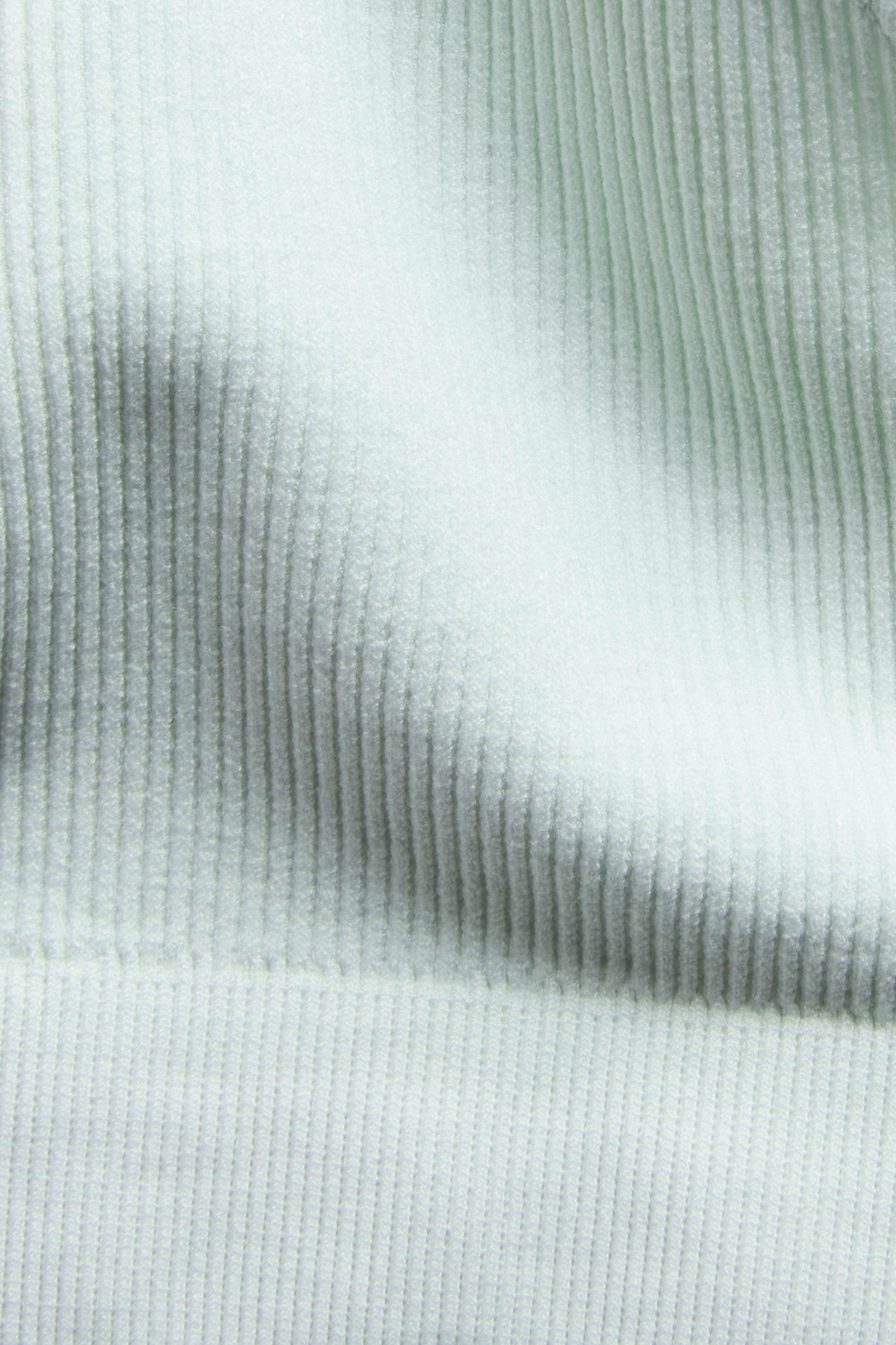 Zbliżenie jasnozielonego bezszwowego prążkowanego topu, pokazujące jego miękką fakturę materiału.