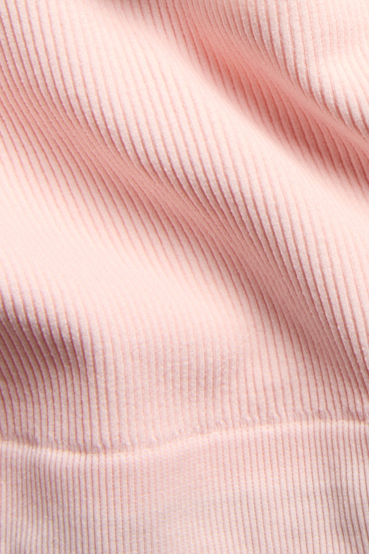 Zbliżenie jasnoróżowego, bezszwowego, prążkowanego materiału topu, ukazujące pionową teksturę.