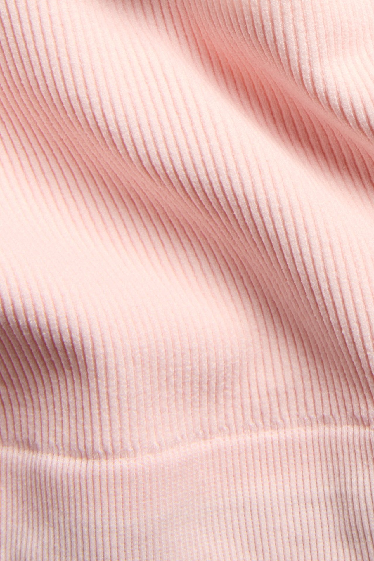 Zbliżenie jasnoróżowego, bezszwowego, prążkowanego materiału topu, ukazujące pionową teksturę.