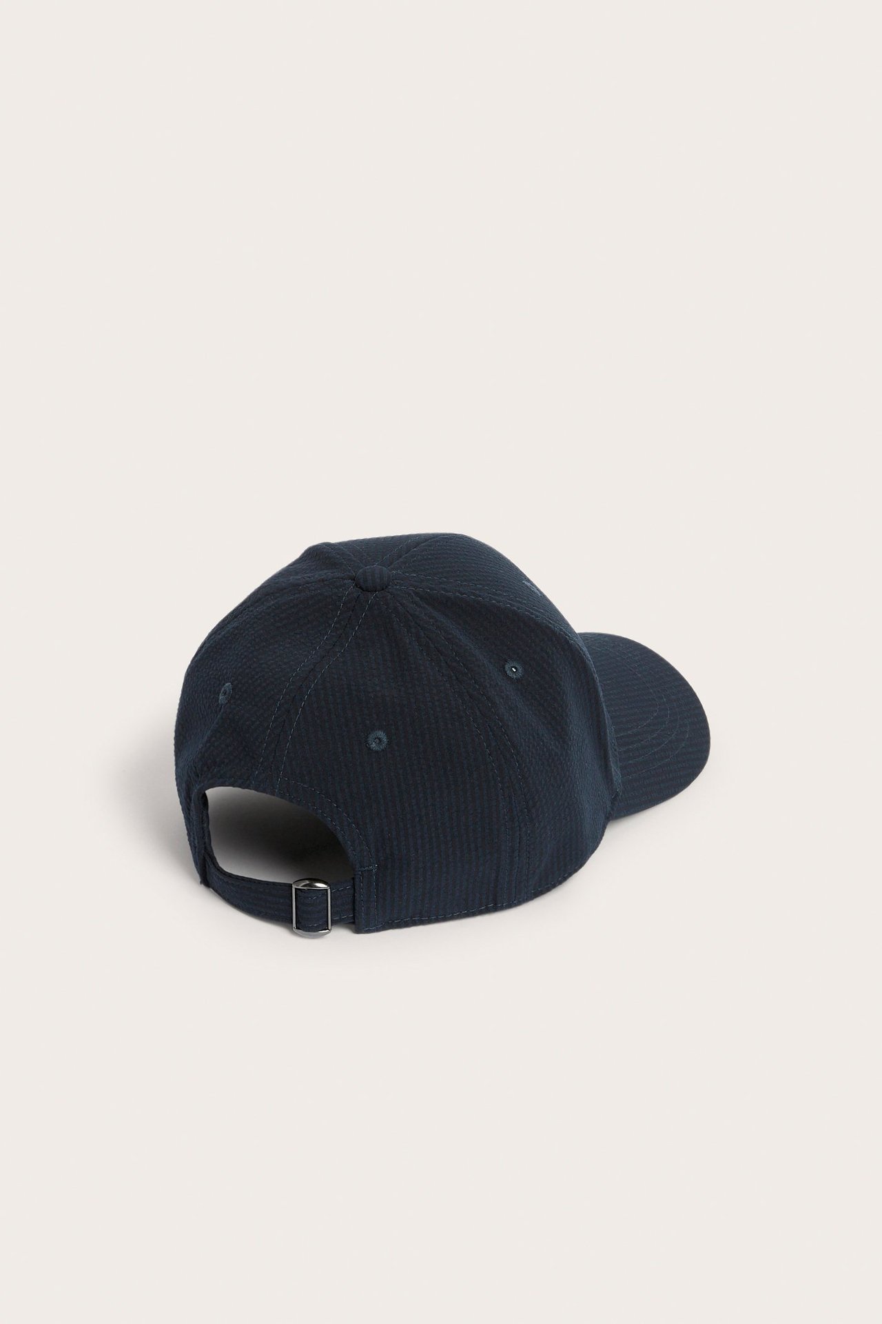 Ryggvy av en mörkblå keps i bäckebölja med ett justerbart spänne baktill.