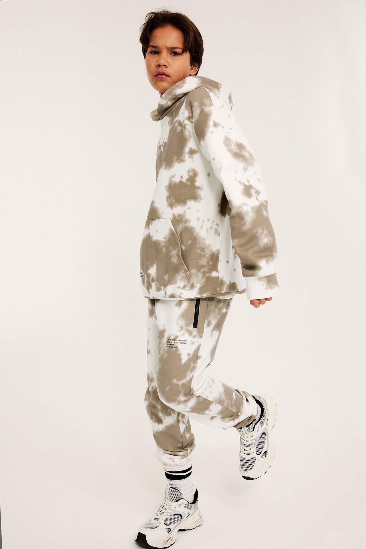 Edestäpäin, lapsi yllään valko-beigen solmuvärjätty huppari ja yhteensopivat collegehousut.