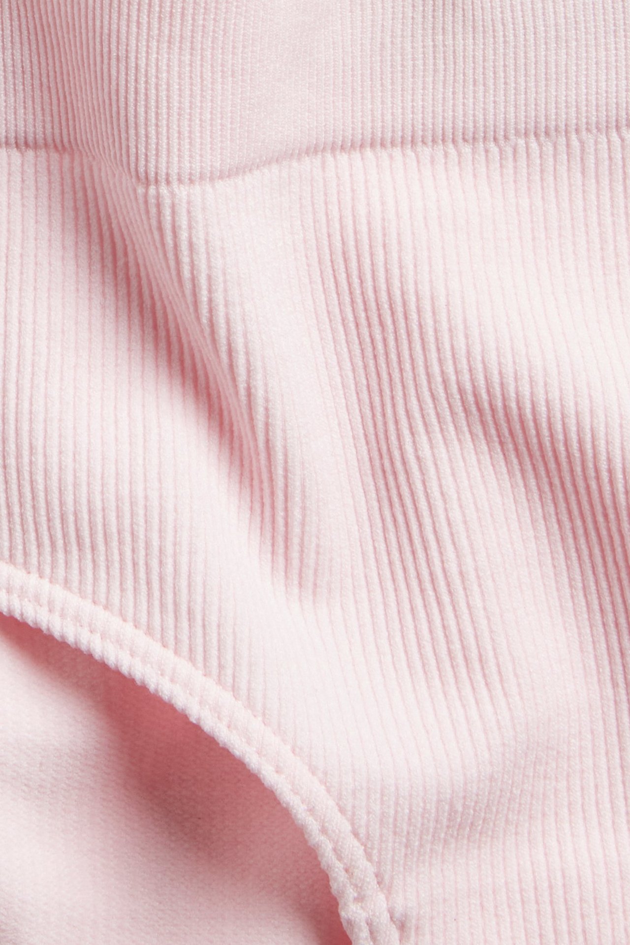 Närbild av rosa sömlösa ribbade hipstertrosor, visar tygets struktur och elastisk kant.