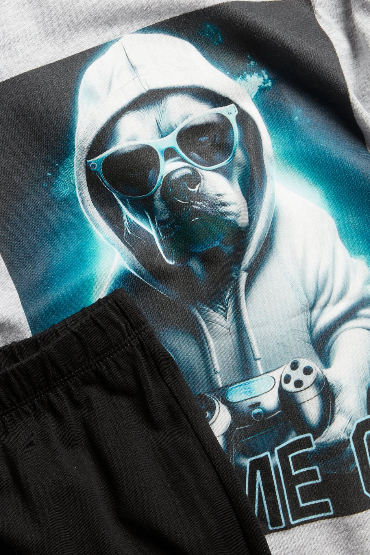 Nærbilde av en lys grå langermet bomullspyjamas til barn med hundetrykk og svart bukse.