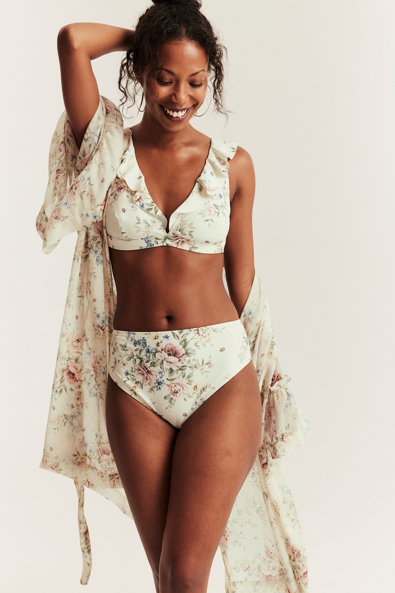 Widok z przodu: kobieta w kremowym kwiecistym topie bikini z falbankami, pasujących figach i zwiewnym kimonie.