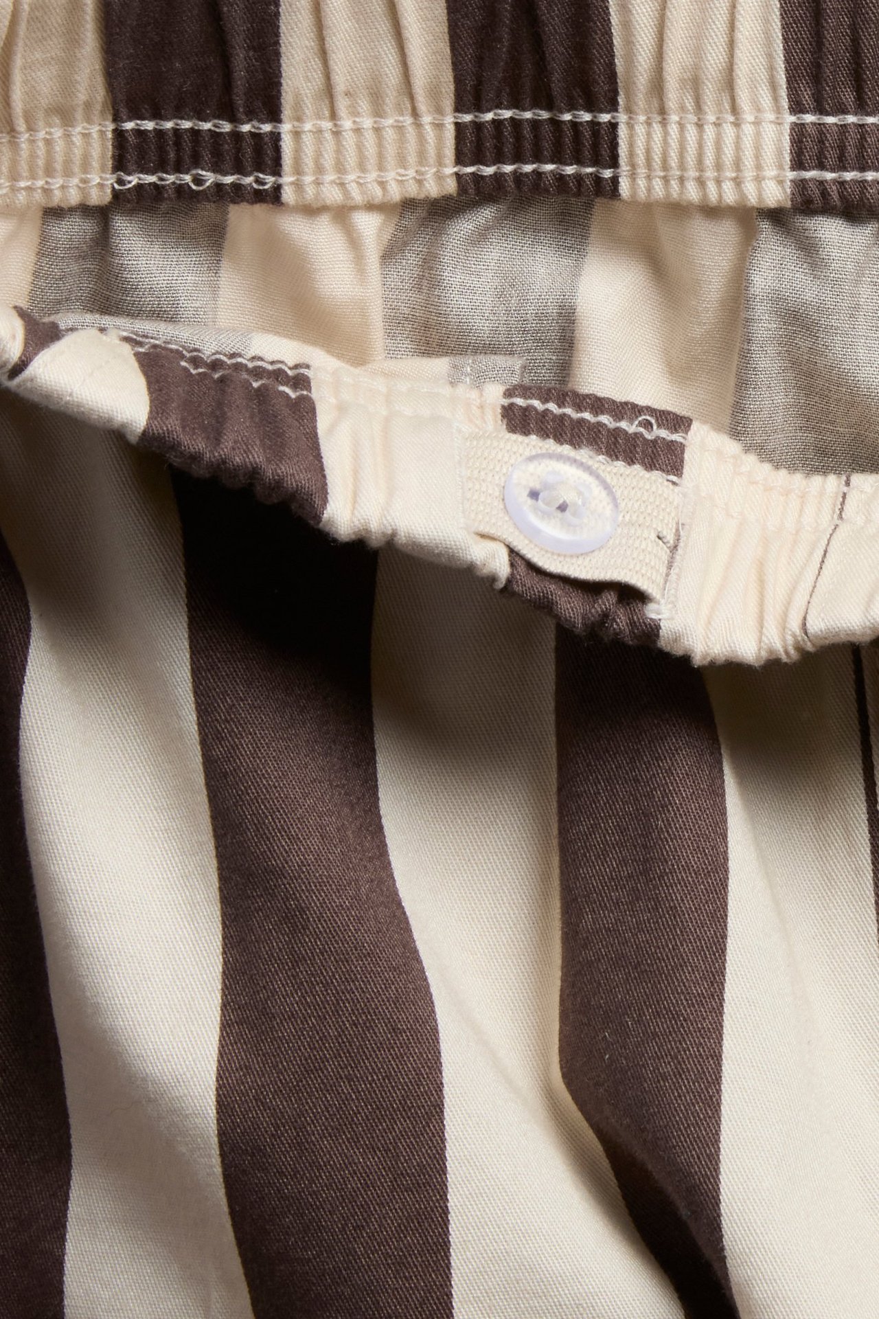 Nærbilde av brune og beige stripete bomullsmykisbukser med justerbar elastisk linning og knapp.