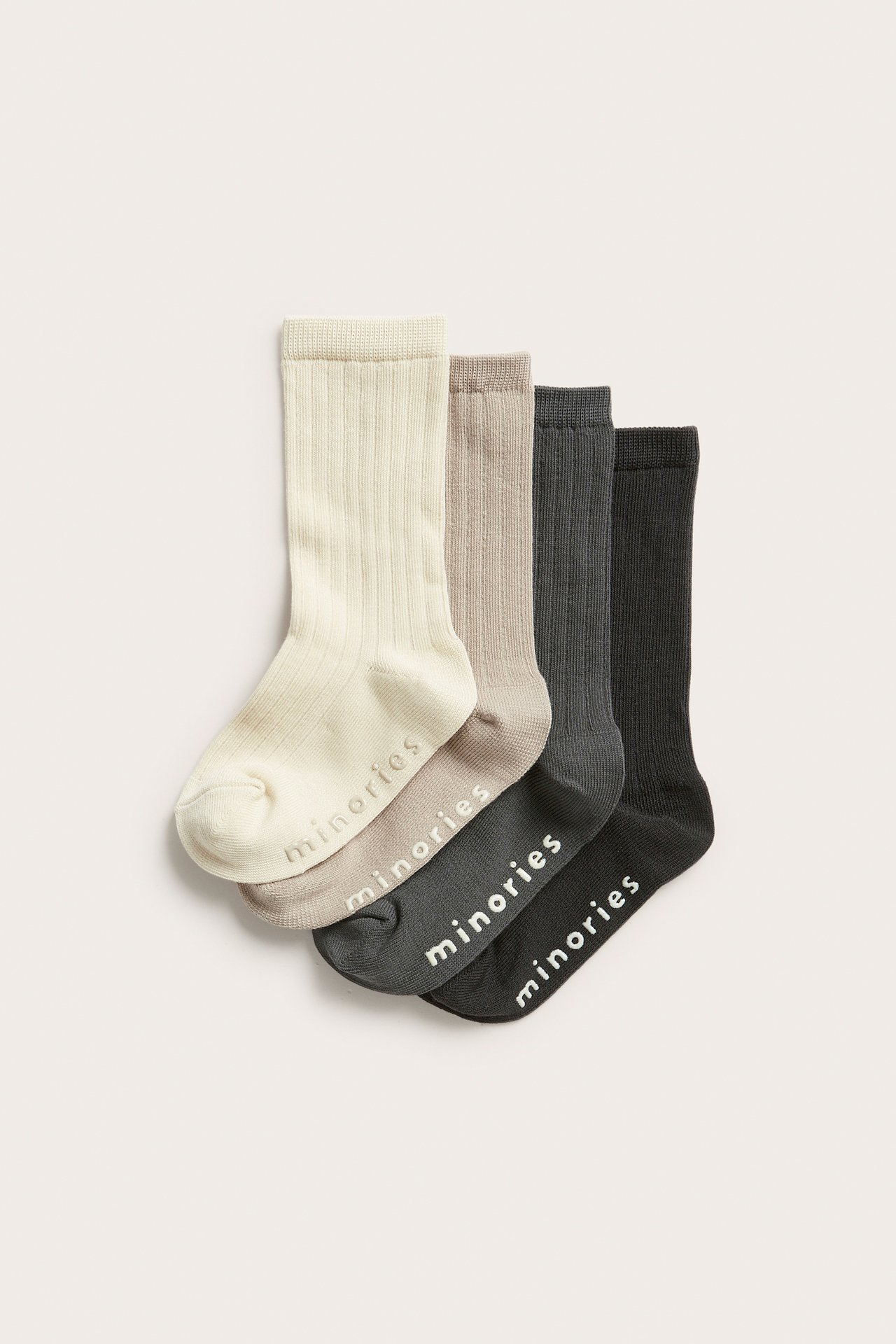 Frontvy: fyra par ribbade strumpor i benvit, beige, mörkgrå och svart med 'minories' logotyp.