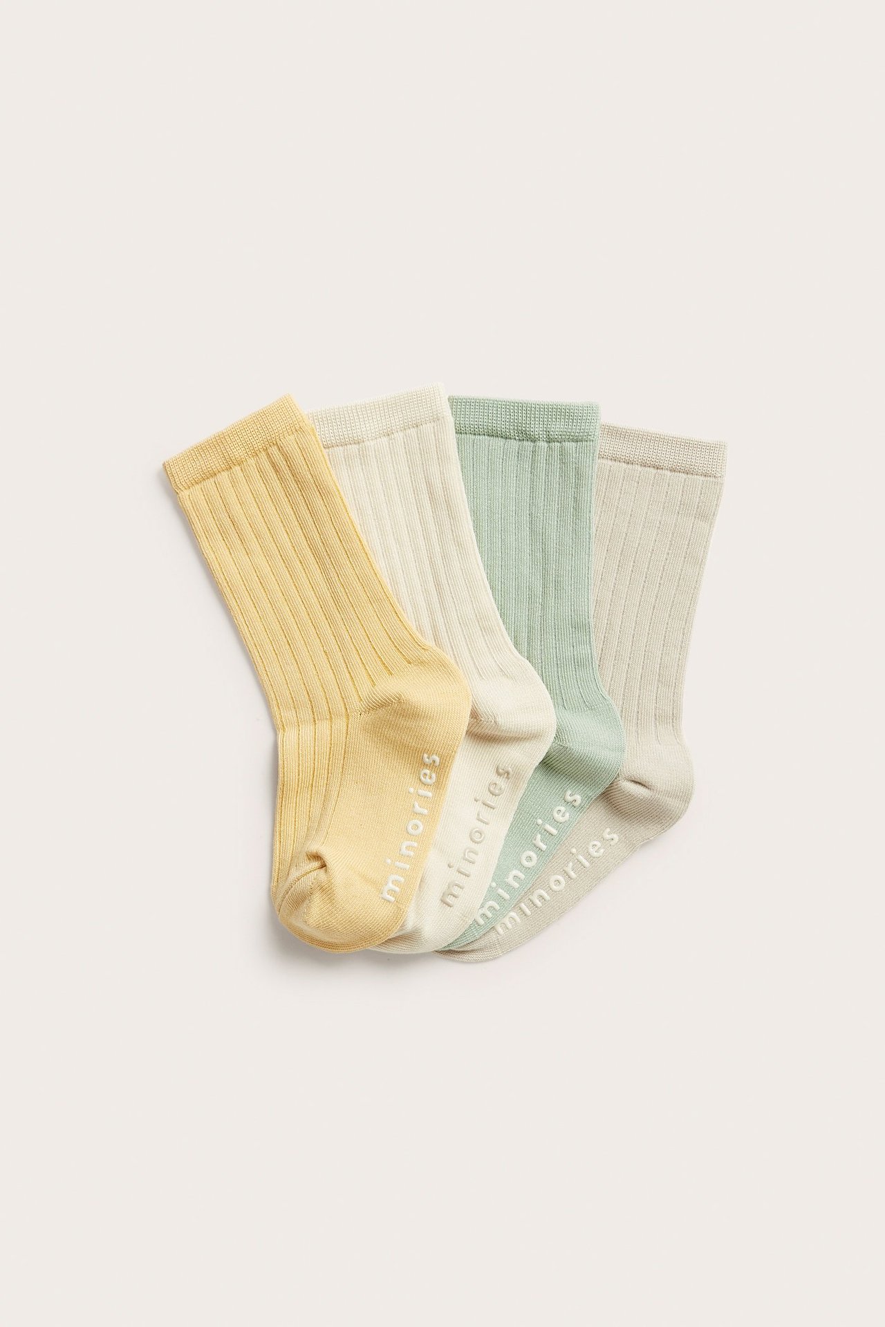 Cztery prążkowane skarpetki: żółte, ecru, jasnozielone, jasnobeżowe, z antypoślizgowymi logami 'minories'.