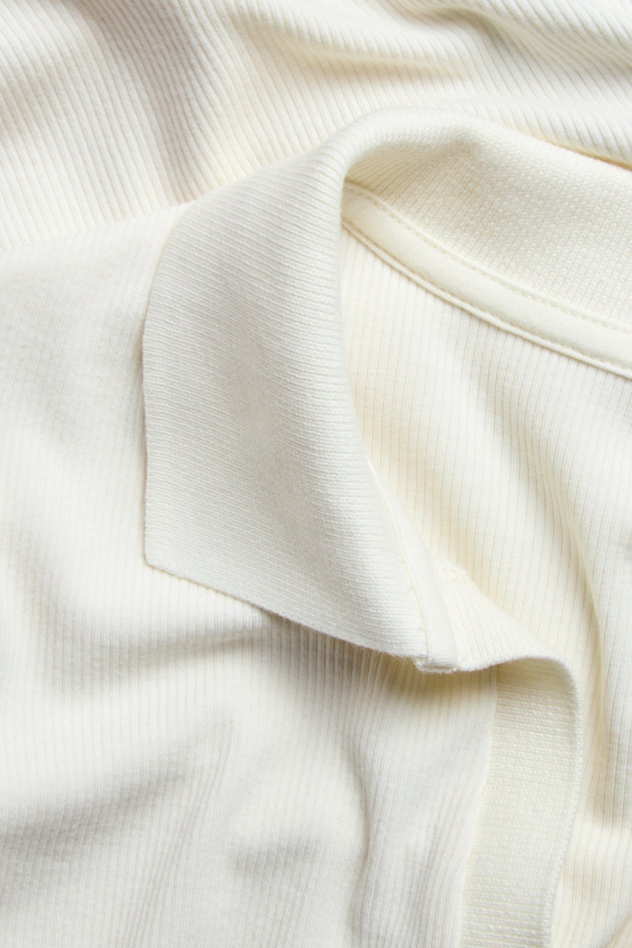 Zbliżenie na kremowy prążkowany top z krótkim rękawem i kołnierzykiem polo.