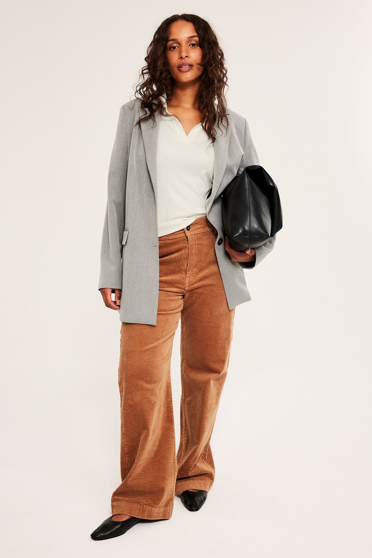 Widok z przodu: Kobieta w kremowym krótkim topie polo, szarym blazerze, brązowych sztruksach, z czarną torebką.