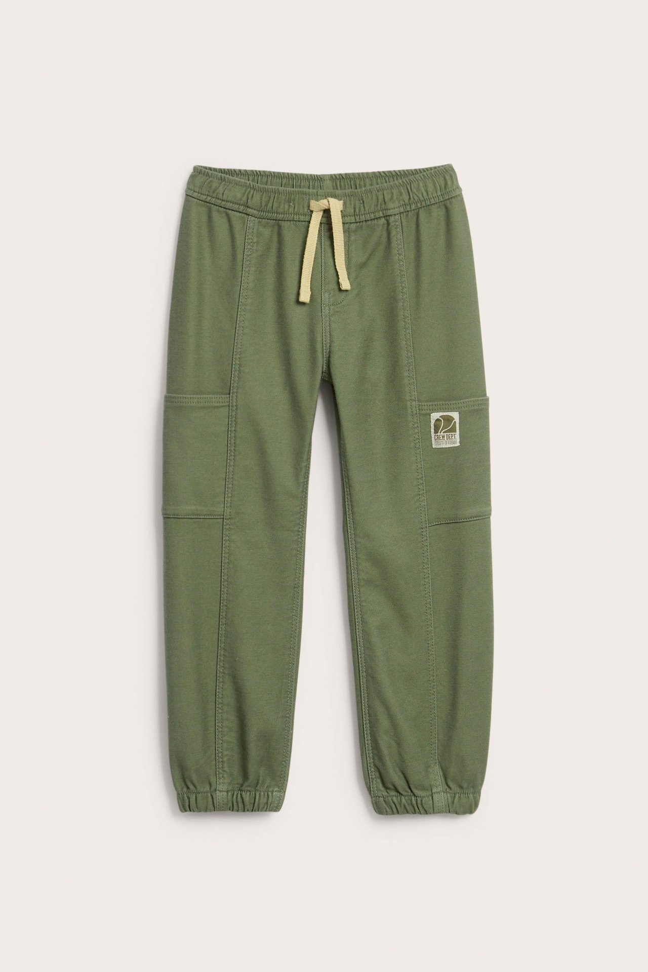 Frontvy av mörkgröna mjukisbyxor för barn med resårmidja, beige dragsko och fickor.