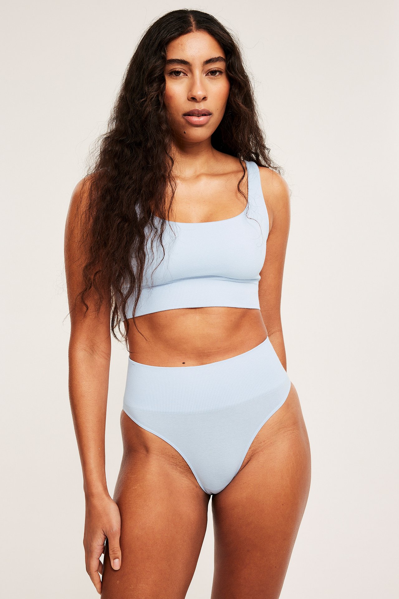 Forfra: Kvinne i lyseblå sømløs Brazilian-truse med ribbet midje og matchende bralette.