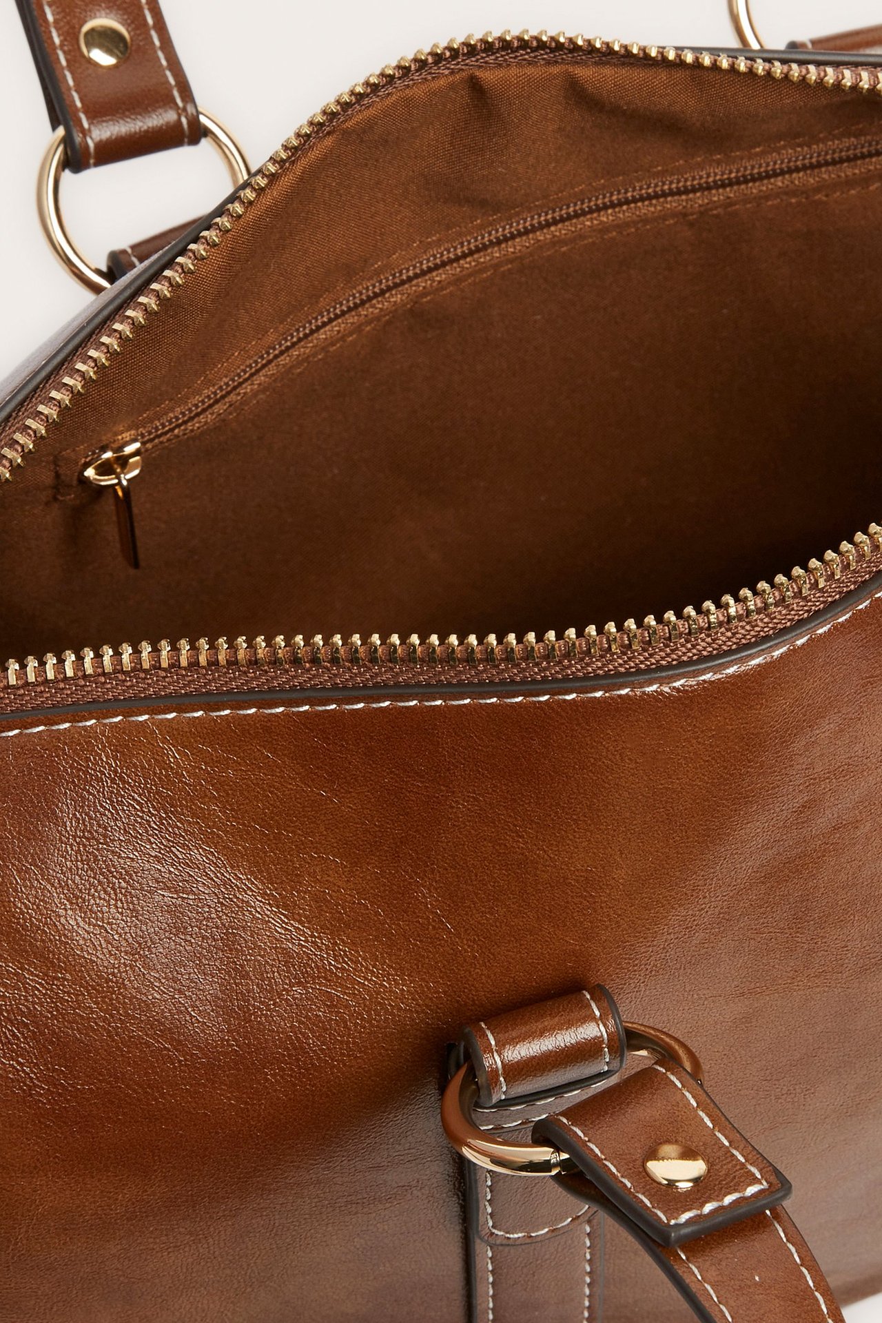 Zbliżenie otwartej brązowej torebki z zamkiem błyskawicznym w kolorze złotym, brązową podszewką i białymi przeszyciami.