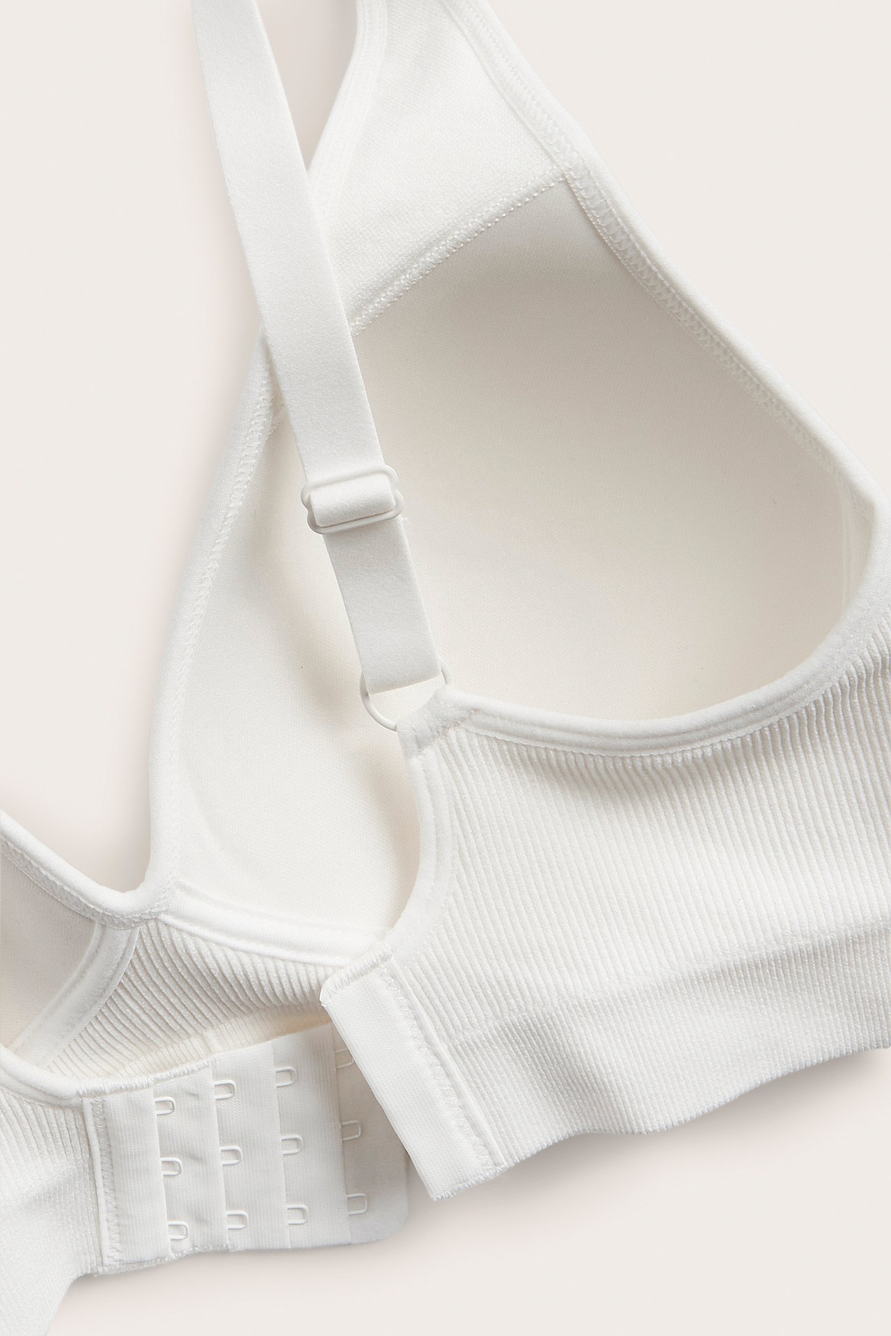 Lähikuva valkoisista saumattomista ribatusta rintaliiveistä muotoilluilla kupeilla ja hakaskiinnityksellä.