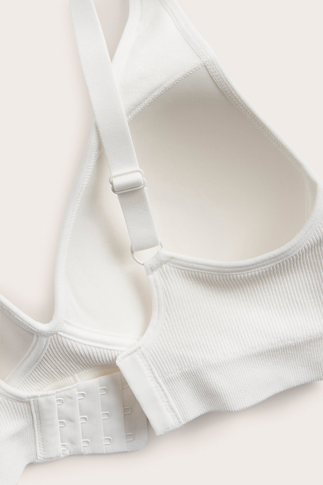 Lähikuva valkoisista saumattomista ribatusta rintaliiveistä muotoilluilla kupeilla ja hakaskiinnityksellä.