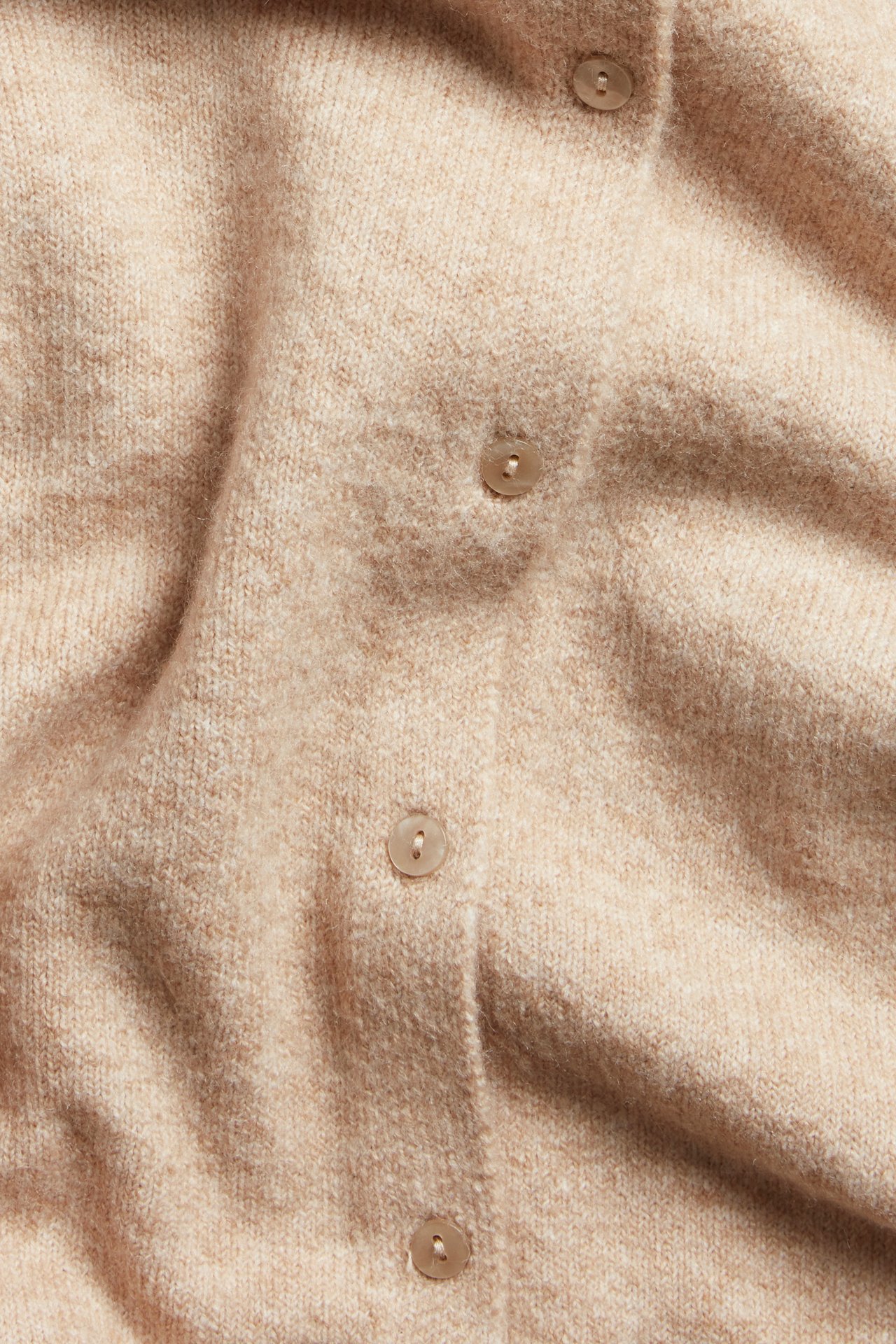 Zbliżenie na melanżowy beżowy materiał kardiganu z guzikami.