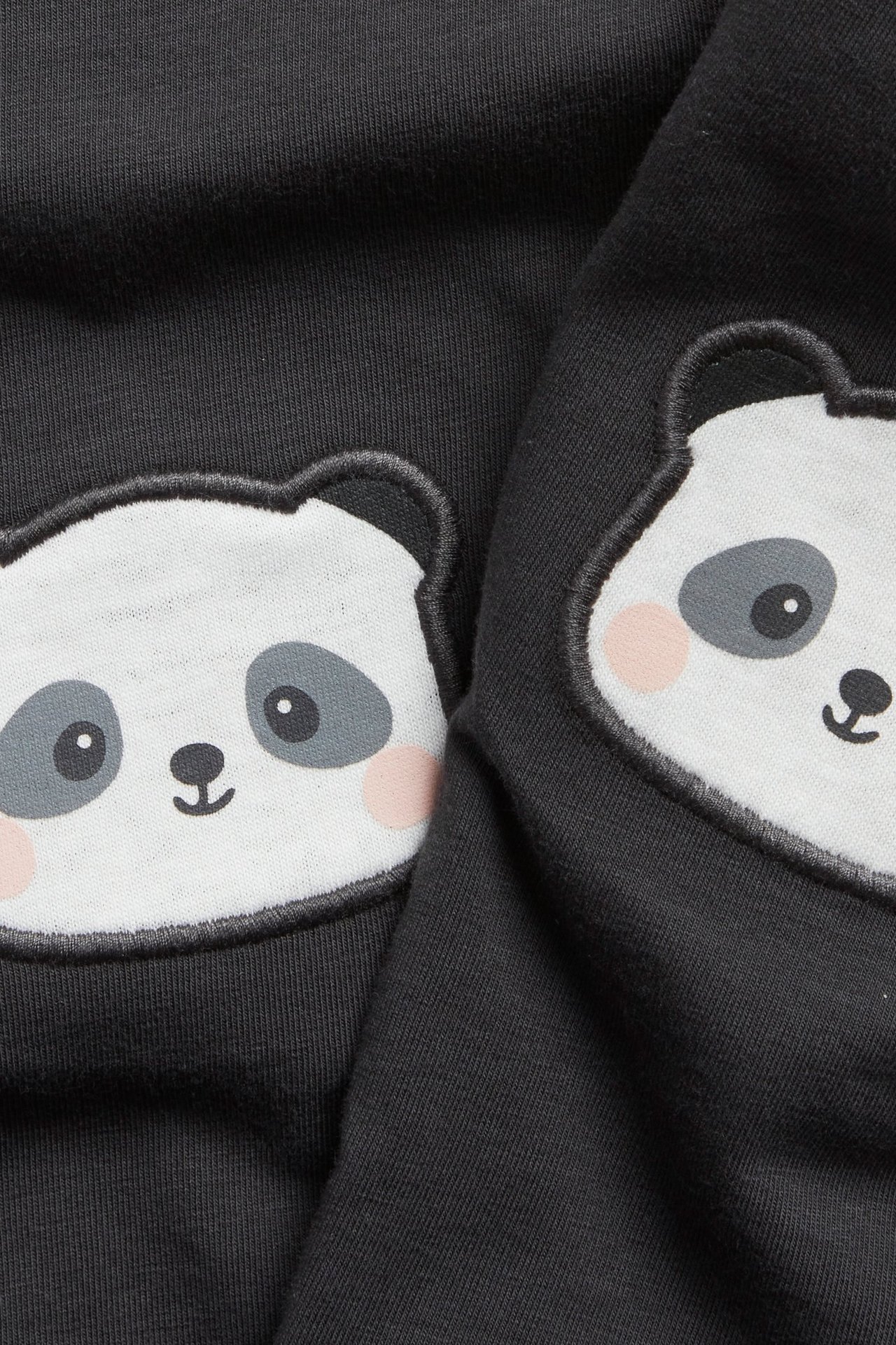 Nærbilde av svarte baby-leggings med hvite panda-applikasjoner på knærne. Myk bomullsblanding.
