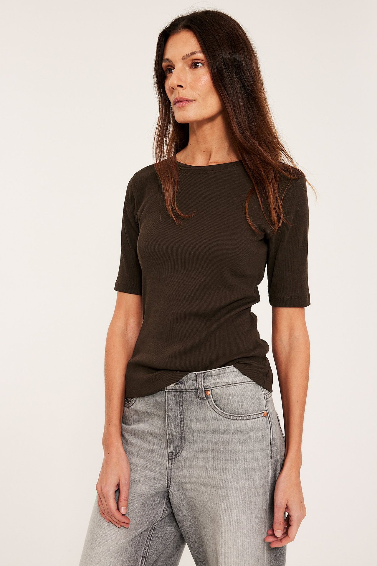 Edestä, nainen tummanruskeassa ribbipaidassa, jossa lyhyet hihat, ja vaaleanharmaissa farkuissa.