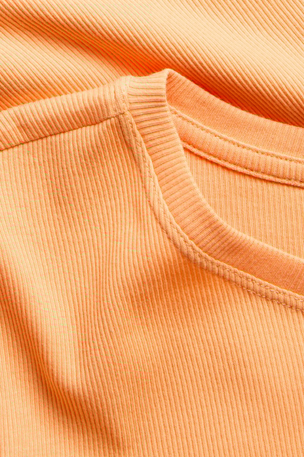 Lähikuva oranssista ribbineulotusta lyhythihaisesta topista, joka esittää sen pyöreää pääntietä.