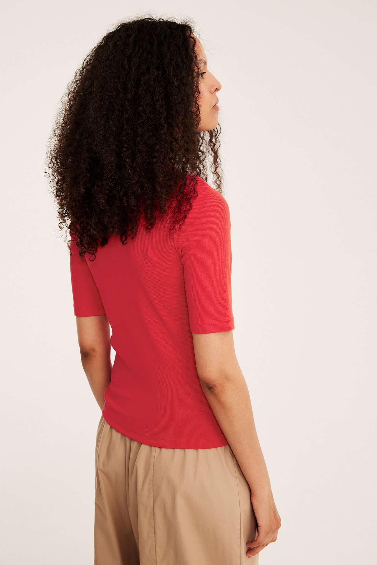 Widok z boku kobiety w czerwonym prążkowanym topie z krótkim rękawem i beżowych spodniach.