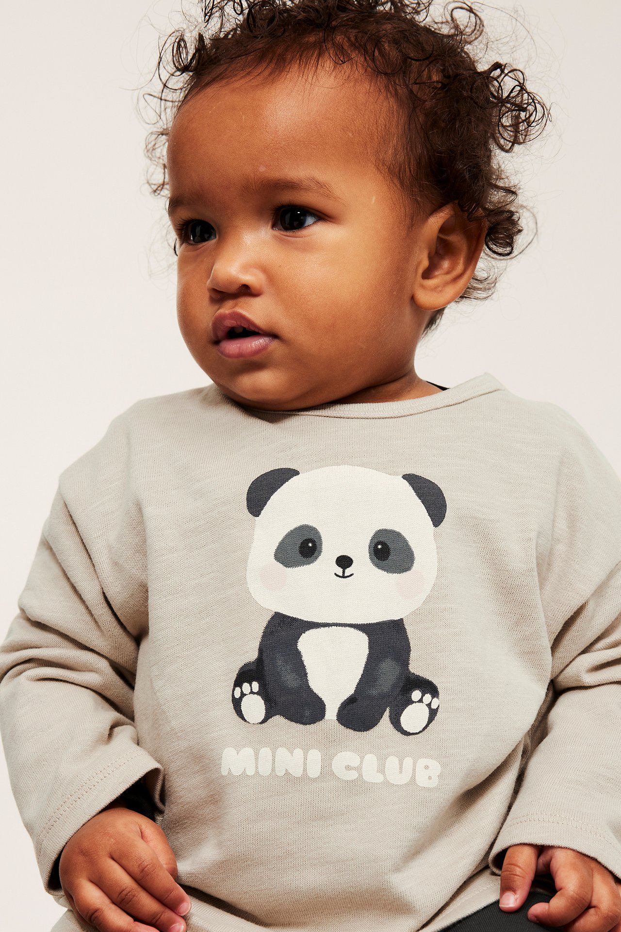 Zbliżenie dziecka w beżowej bawełnianej koszulce z długim rękawem z nadrukiem pandy z przodu.