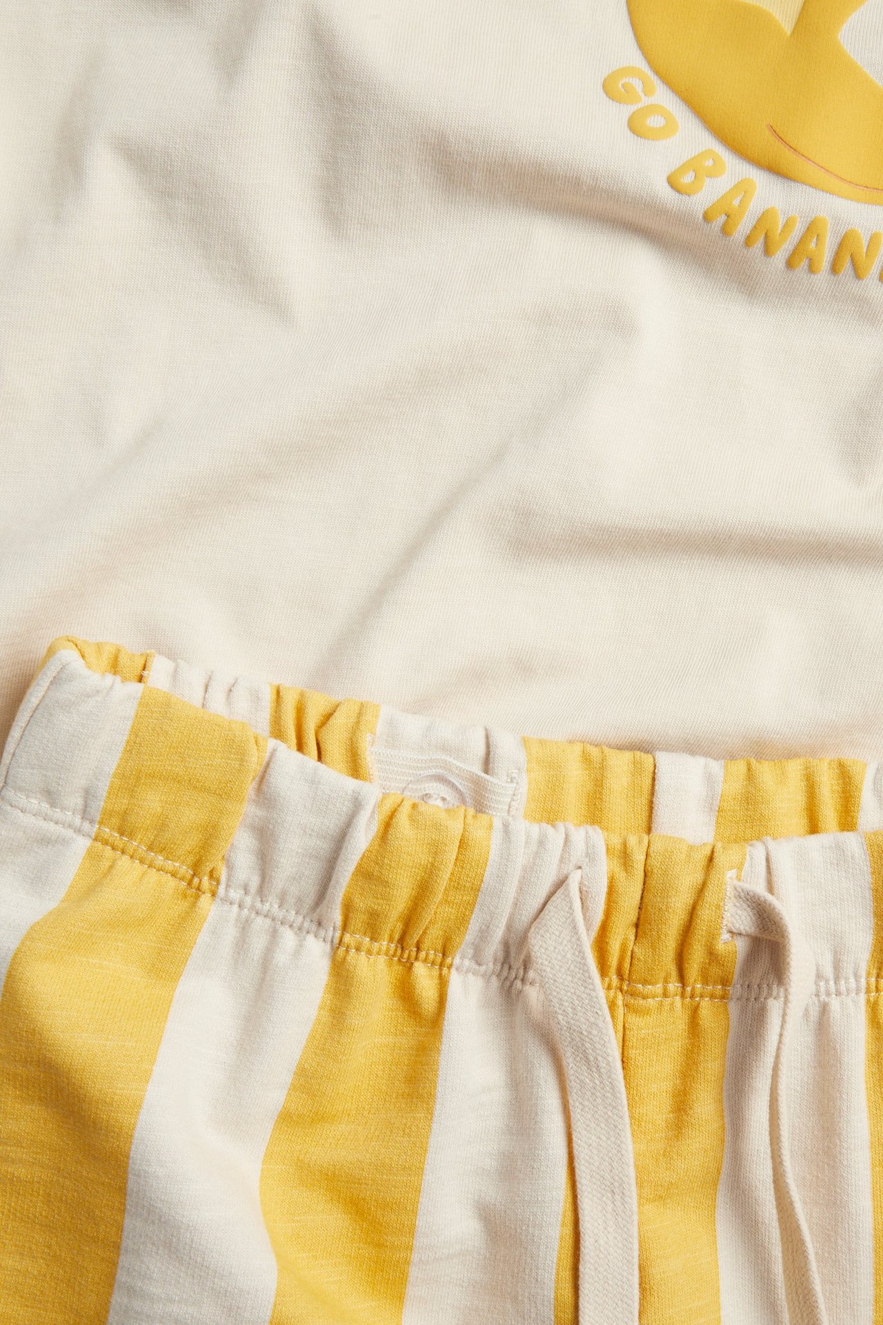 Zbliżenie na żółte pasiaste szorty bawełniane ze sznurkiem i kremowy T-shirt z nadrukiem banana.