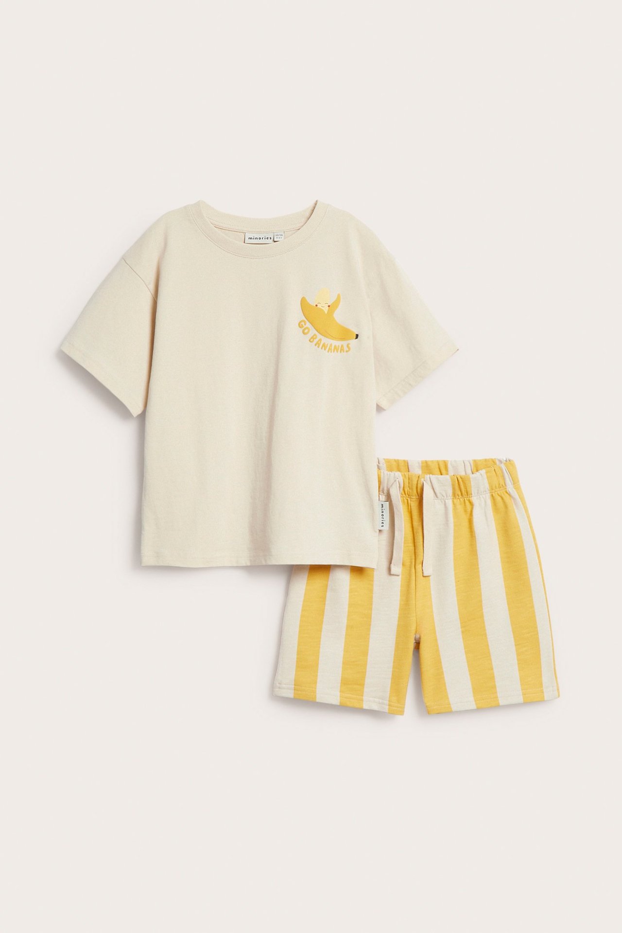 Widok z przodu: Dziecięca beżowa koszulka z nadrukiem banana i żółto-białe szorty w paski ze sznurkiem.