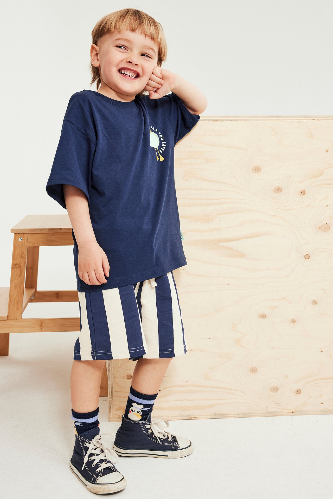 Forfra, en gutt i mørkeblå trykt T-skjorte og stripete shorts-sett med joggesko.