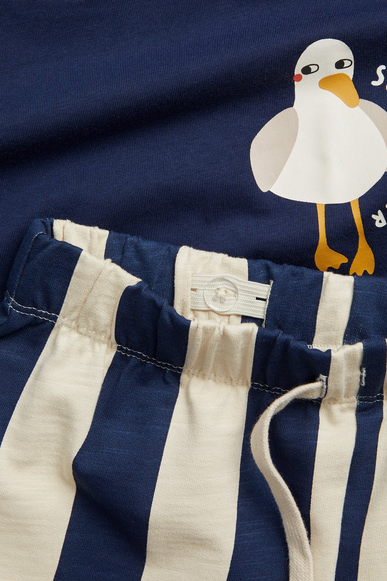 Zbliżenie na dziecięce niebiesko-białe bawełniane szorty w paski ze sznurkiem i niebieską koszulkę z nadrukiem mewy.