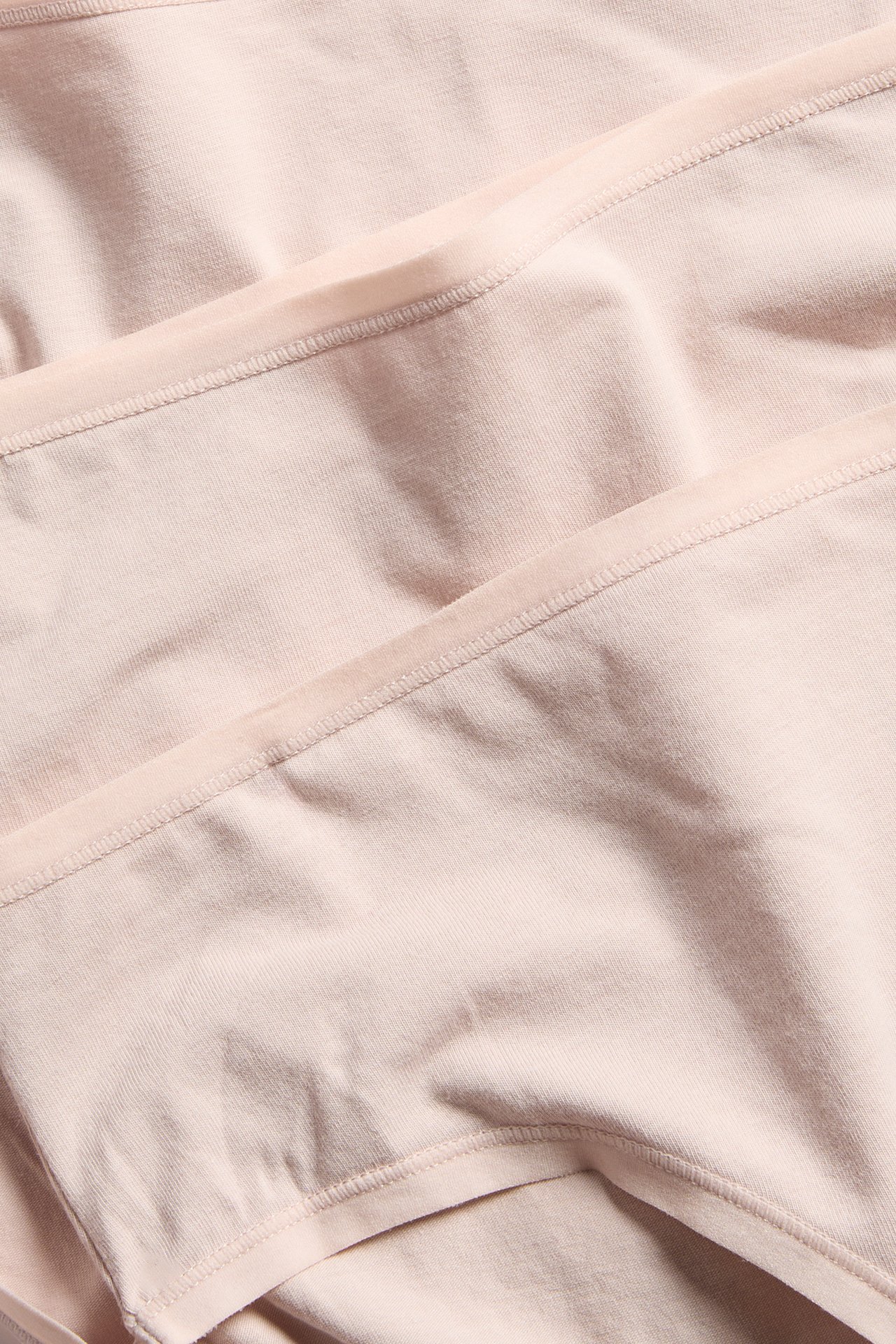 Nærbilde av stablede lyserosa bomullstruser, som viser det ensfargede stoffet og den enkle overkanten.