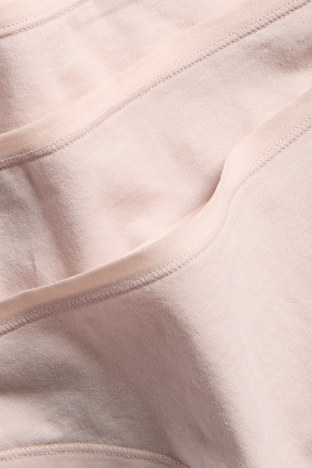 Zbliżenie na jasnoróżowe bawełniane stringi, pokazujące jednolity materiał z widocznymi szwami i fałdami.