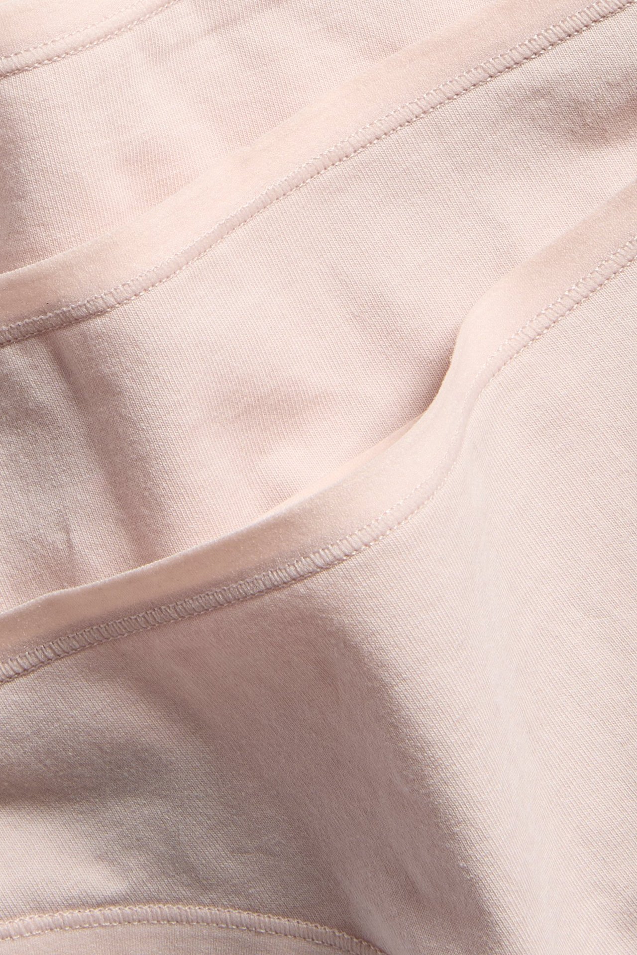 Zbliżenie na jasnoróżowe bawełniane stringi, pokazujące jednolity materiał z widocznymi szwami i fałdami.