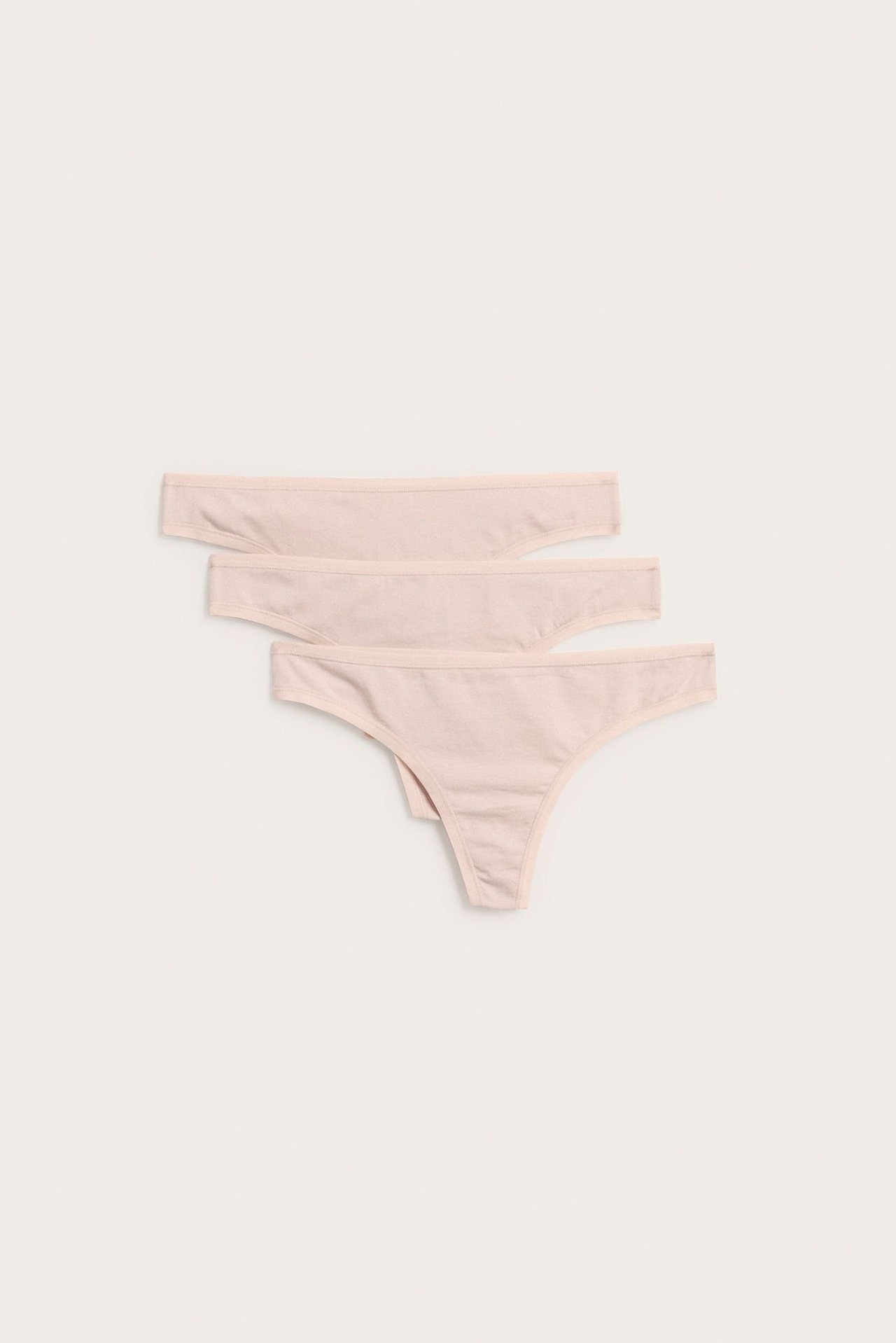 Widok z przodu trzech gładkich jasnoróżowych bawełnianych stringów, ułożonych ukośnie.