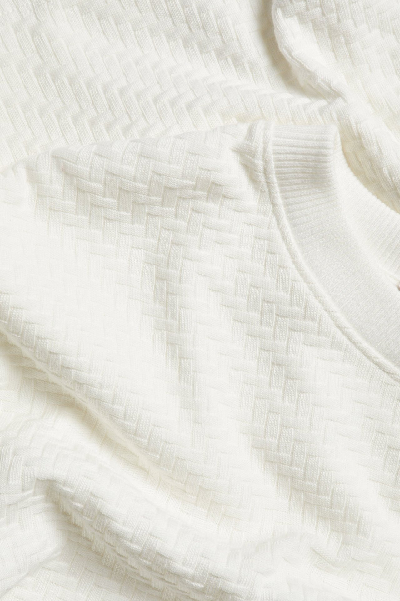 Zbliżenie na biały bawełniany T-shirt z dzianiny o teksturowanym splocie koszykowym i prążkowanym dekolcie.