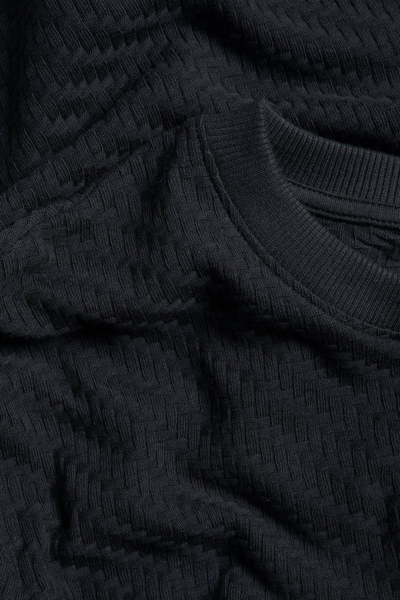 Zbliżenie czarnego bawełnianego T-shirtu ze strukturalnym wzorem i prążkowanym dekoltem.